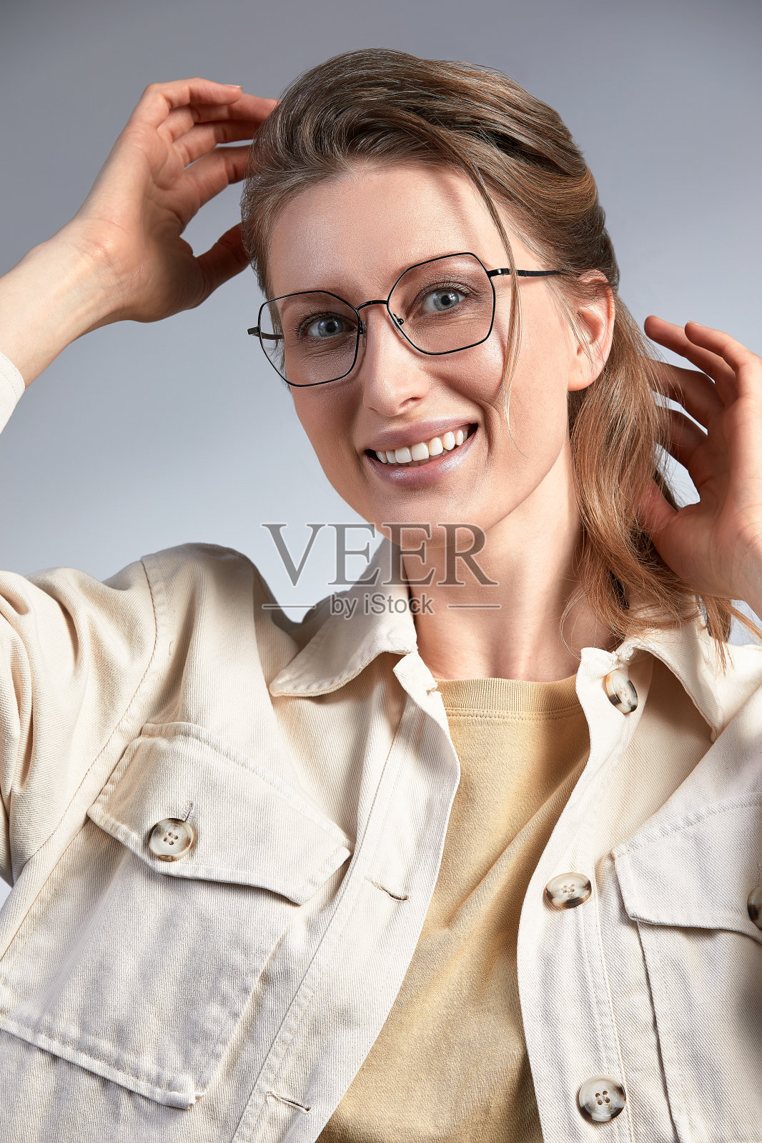 一个美丽的穿着时髦的中年妇女，戴着时髦的眼镜，微笑着对着镜头摆姿势，一个35-45岁的金发女人，灰色背景下戴着眼镜，皮肤健康照片摄影图片