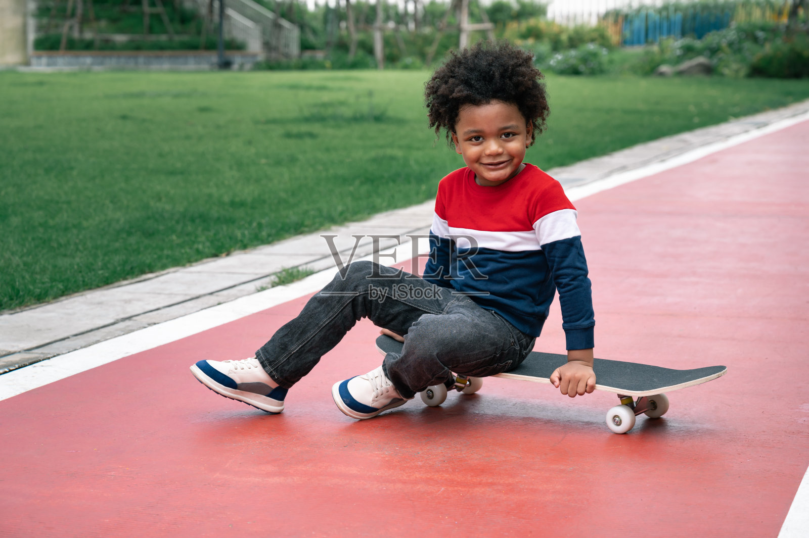 在公园里玩滑板，一头非洲式发型的快乐小男孩照片摄影图片
