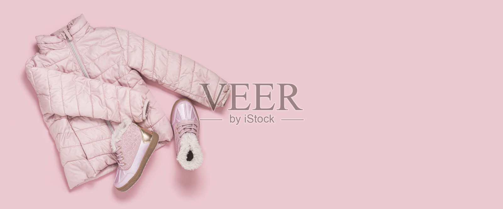 粉红色背景上的小女孩的儿童夹克和靴子。俯视图，平躺。横幅。照片摄影图片