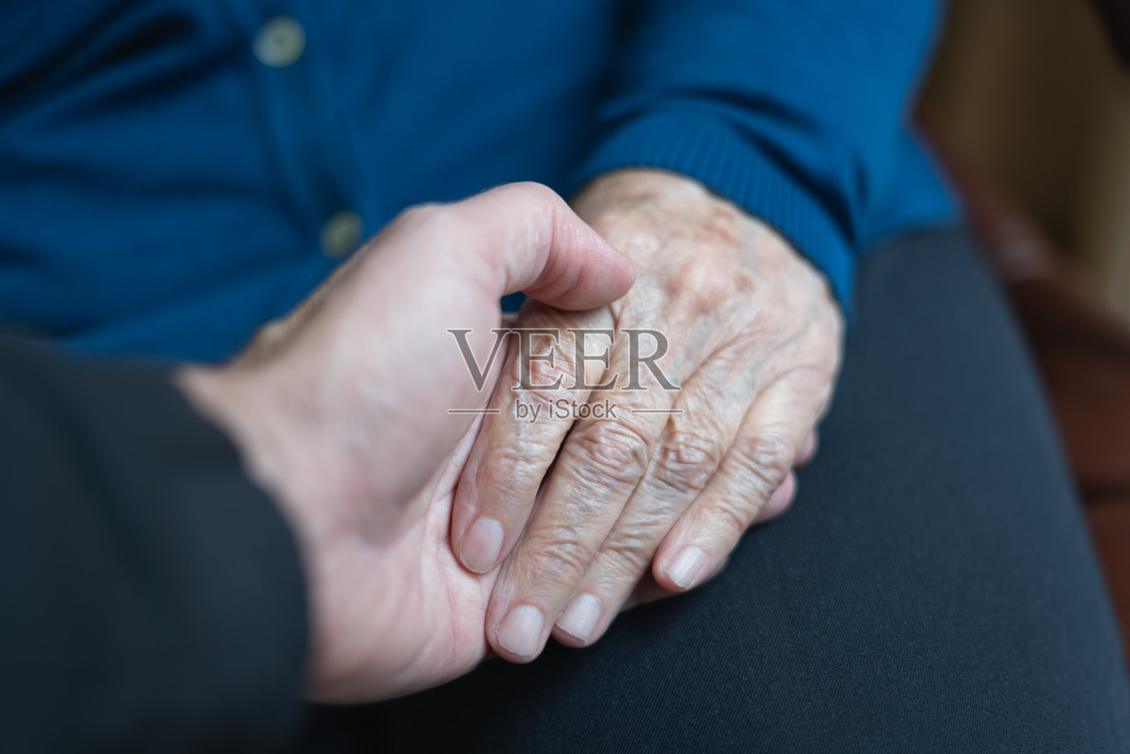 年轻男人的手牵着年长女人的手，以关怀和帮助的态度。照片摄影图片