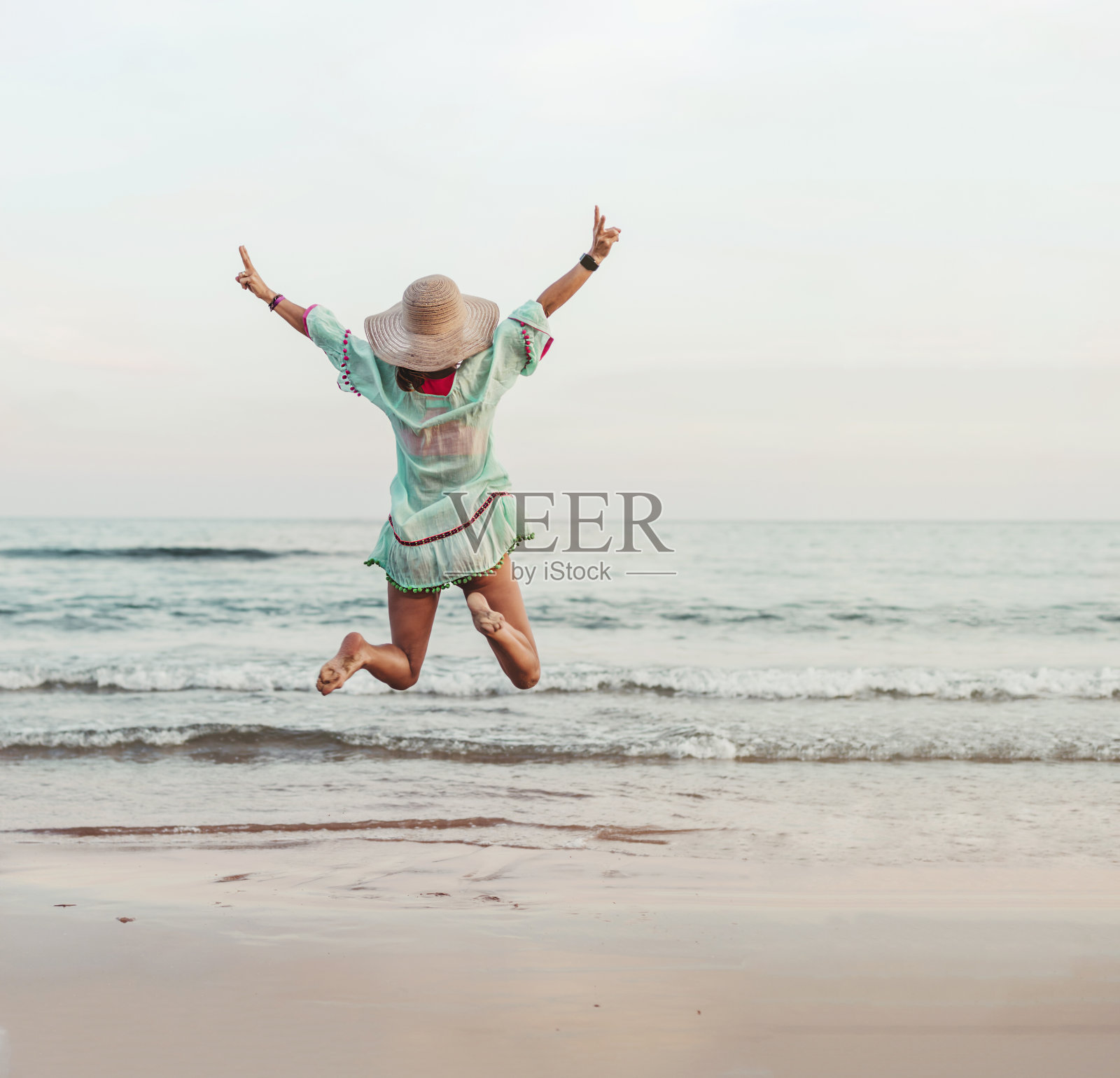 一个穿着绿色衣服的女人在海边跳着，一边望着海浪。她是快乐的。她在庆祝什么。实现目标和幸福的概念。照片摄影图片
