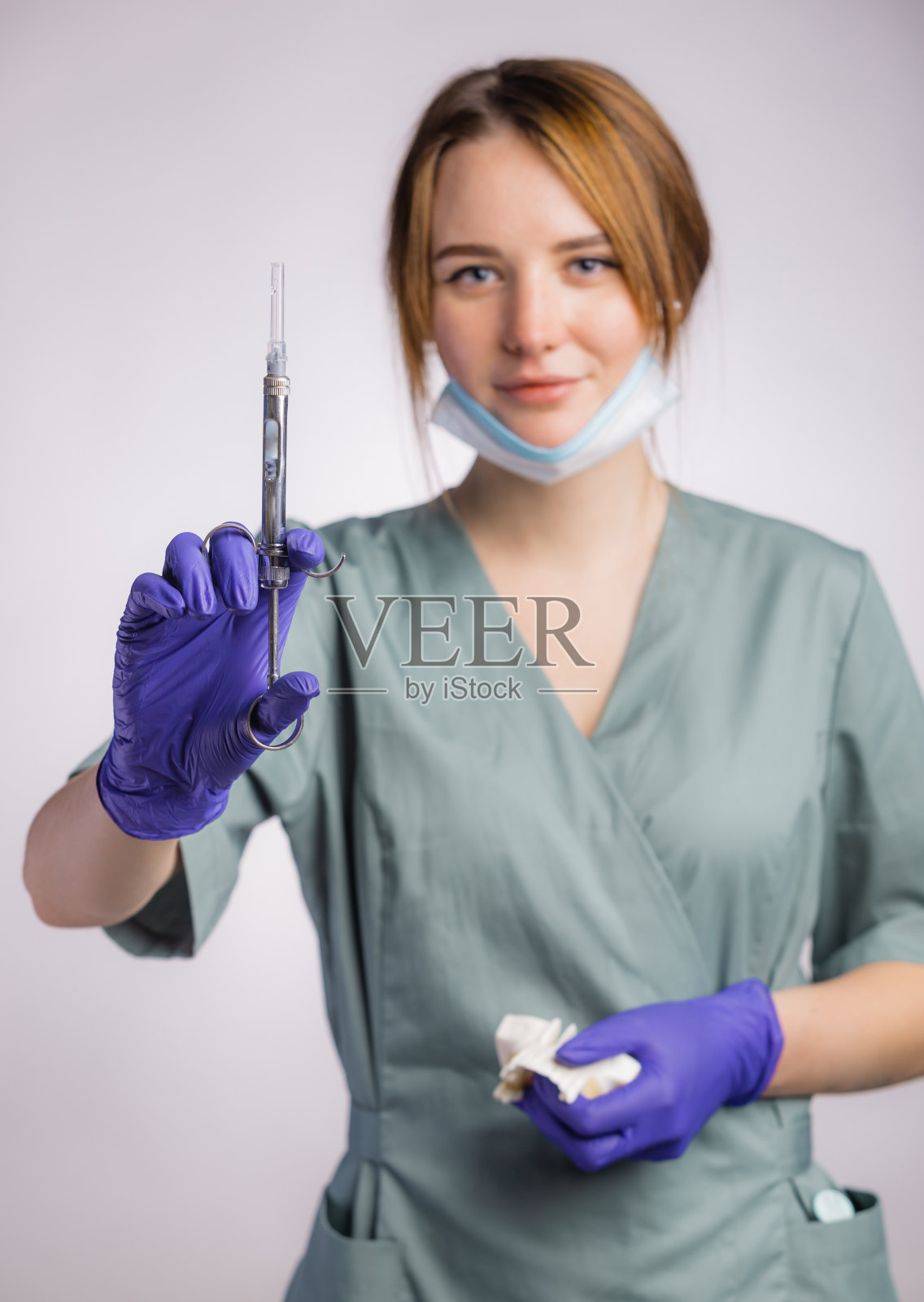 灰色背景下，漂亮的女牙医手持注射器注射器，戴着统一的医用口罩和乳胶医用手套照片摄影图片