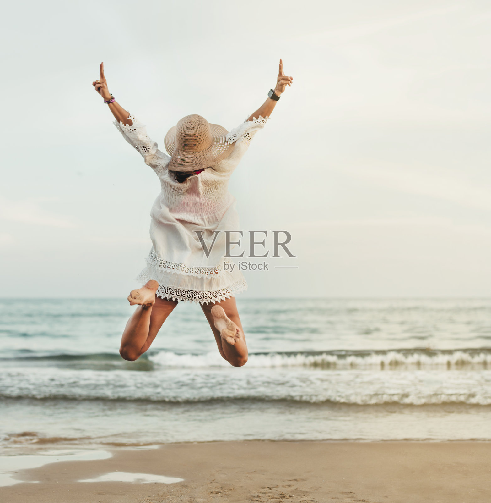 一个戴着草帽的女人在海滩上跳着，望着大海。她仰卧着。概念幸福和假期。照片摄影图片
