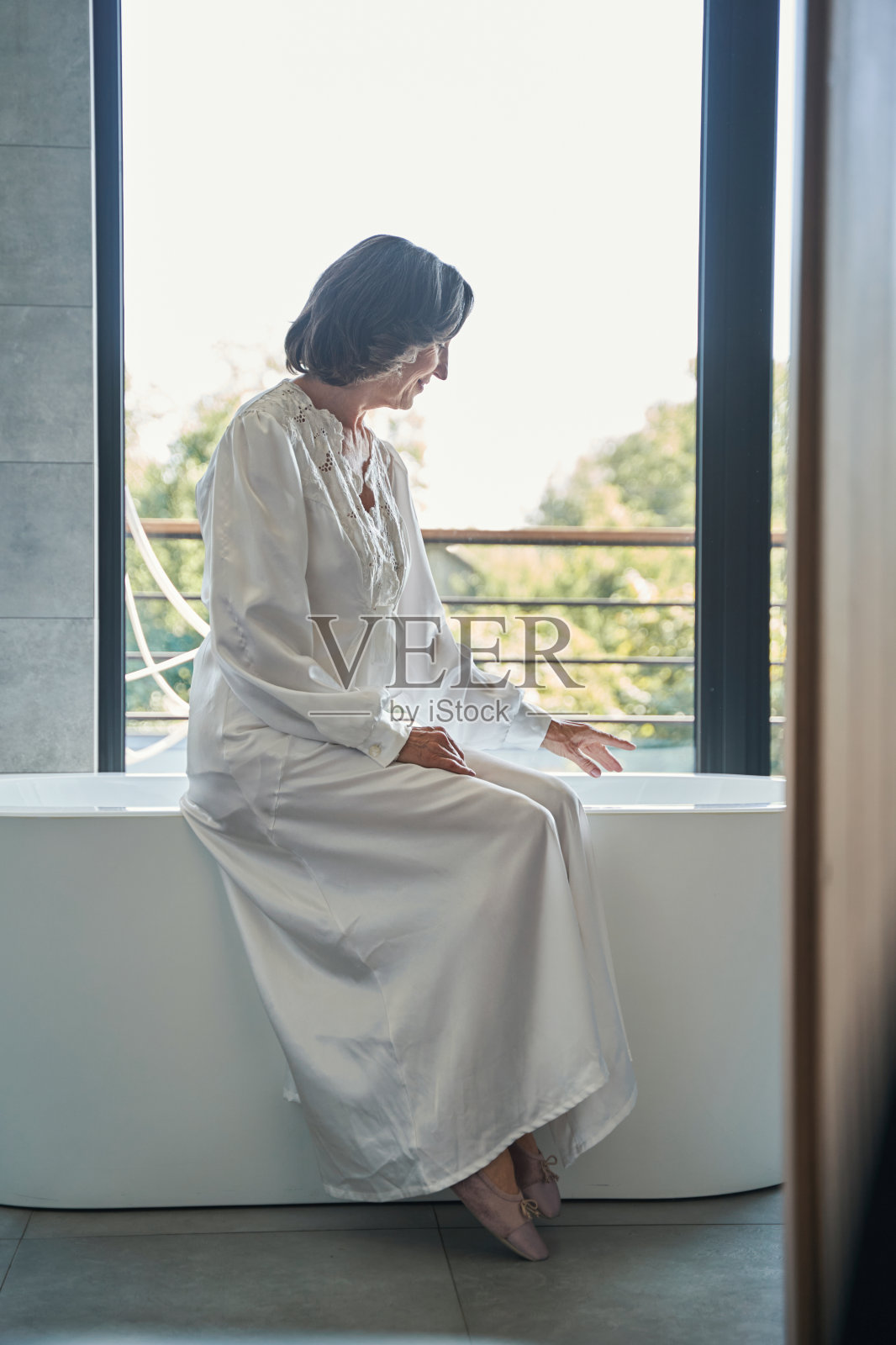 一位上了年纪的女士正在检查浴缸的水温照片摄影图片