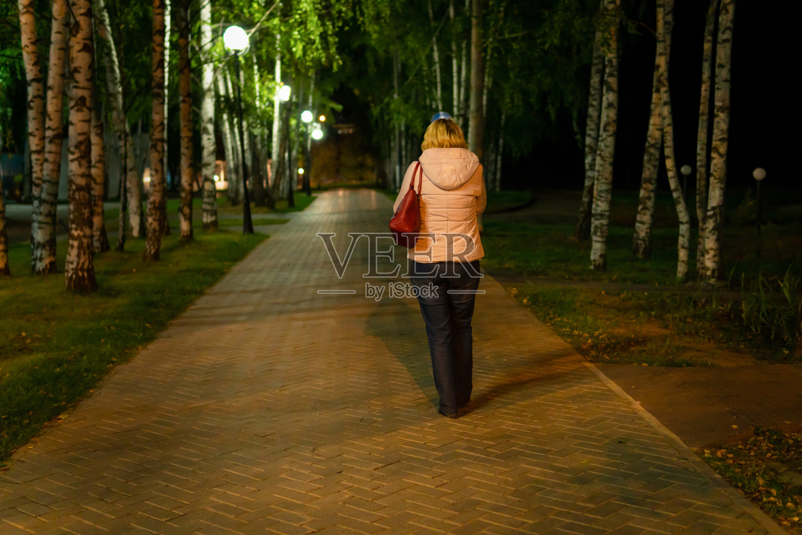 一个女人手里拿着手机走在夜城里。照片摄影图片