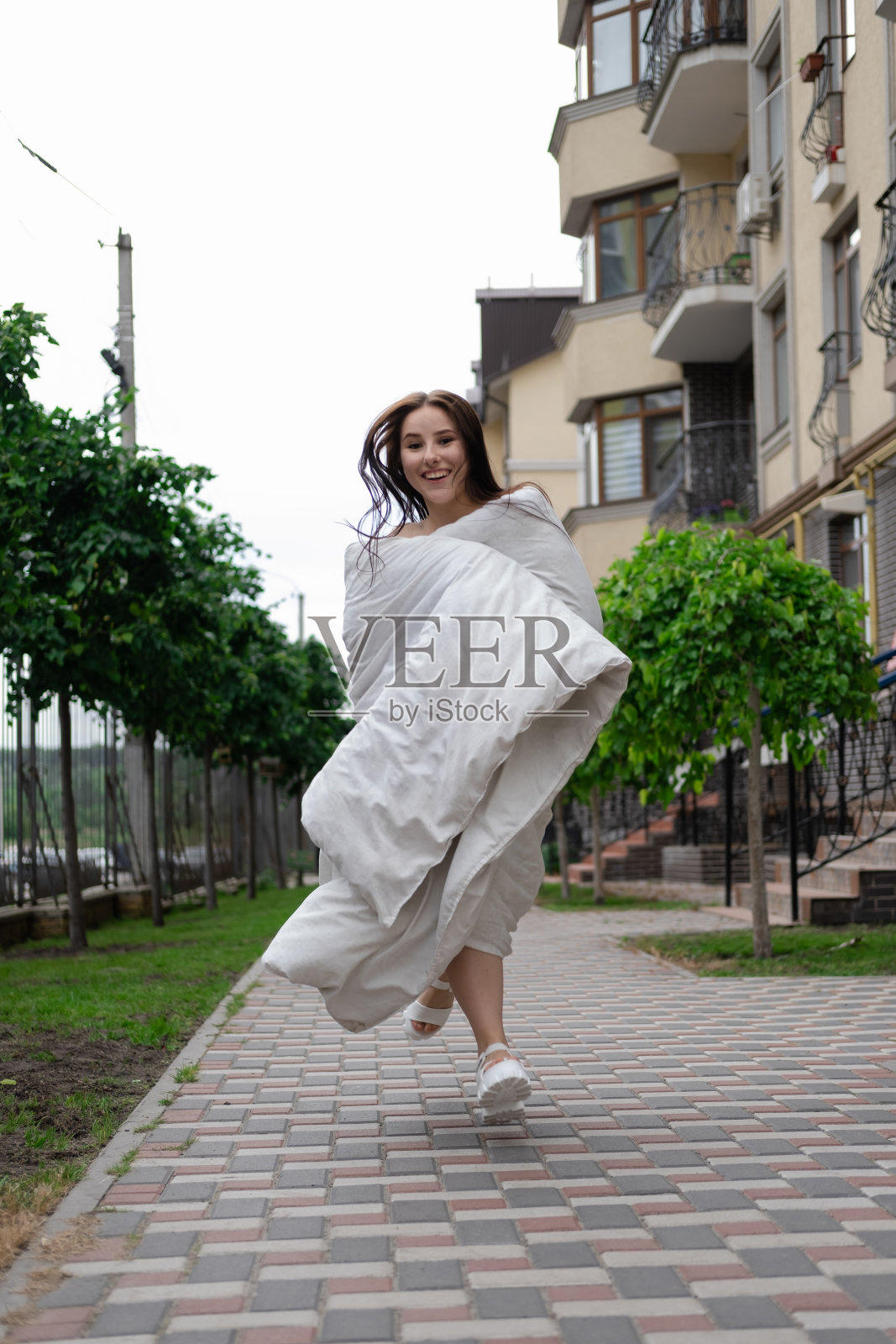 漂亮的黑发女人，裹着白毯子在街上。疯狂美丽的千禧一代无忧无虑的女孩照片摄影图片