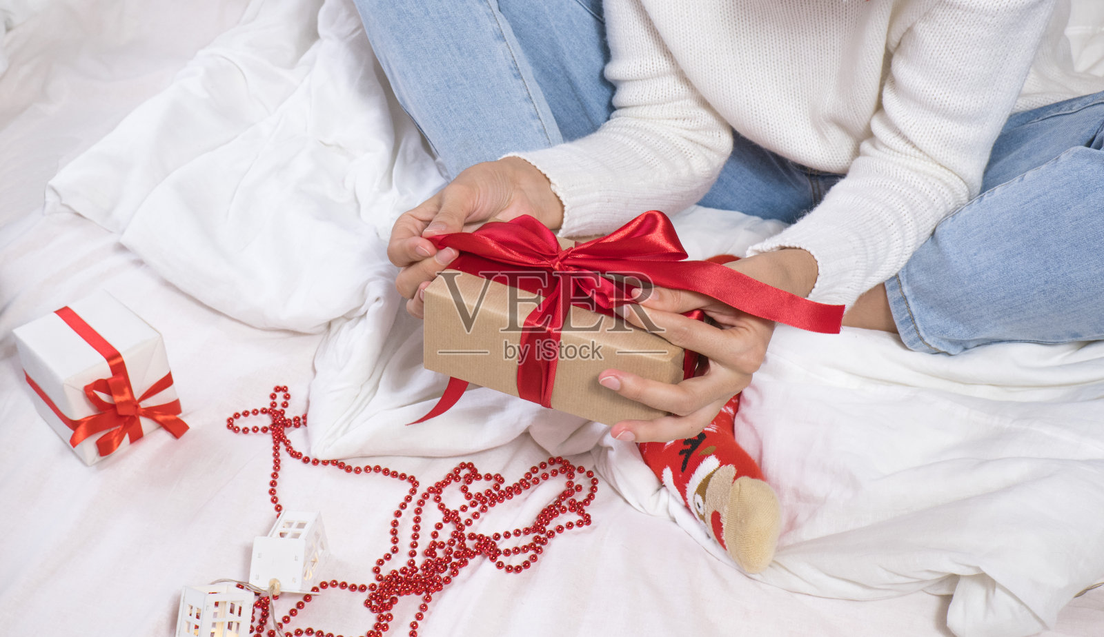 一个戴着圣诞老人帽子的黑发年轻女人，躺在白色的床上，打开一个圣诞礼物盒。圣诞礼物。照片摄影图片