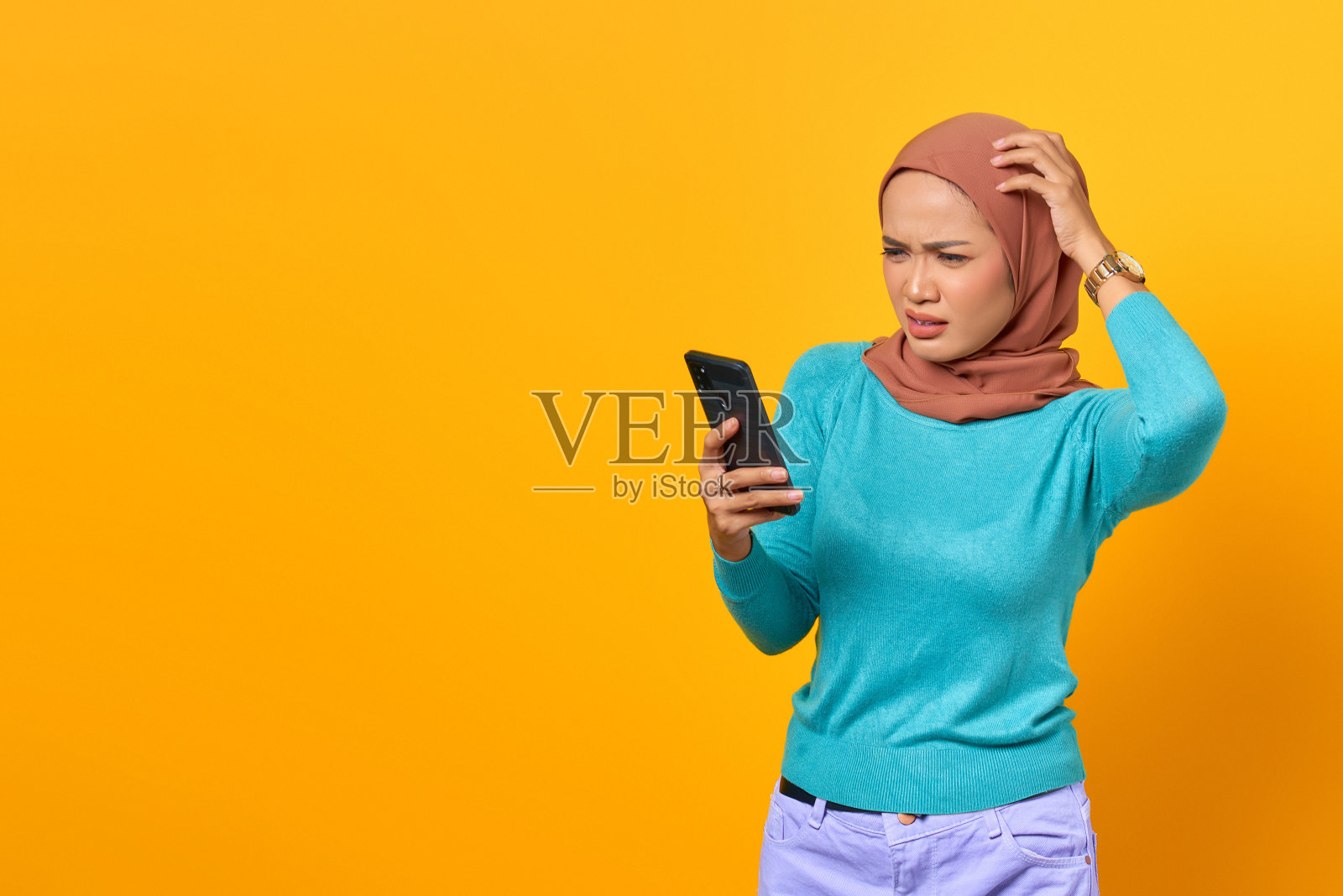 一名年轻的亚洲女性震惊地看着黄色背景的智能手机屏幕照片摄影图片