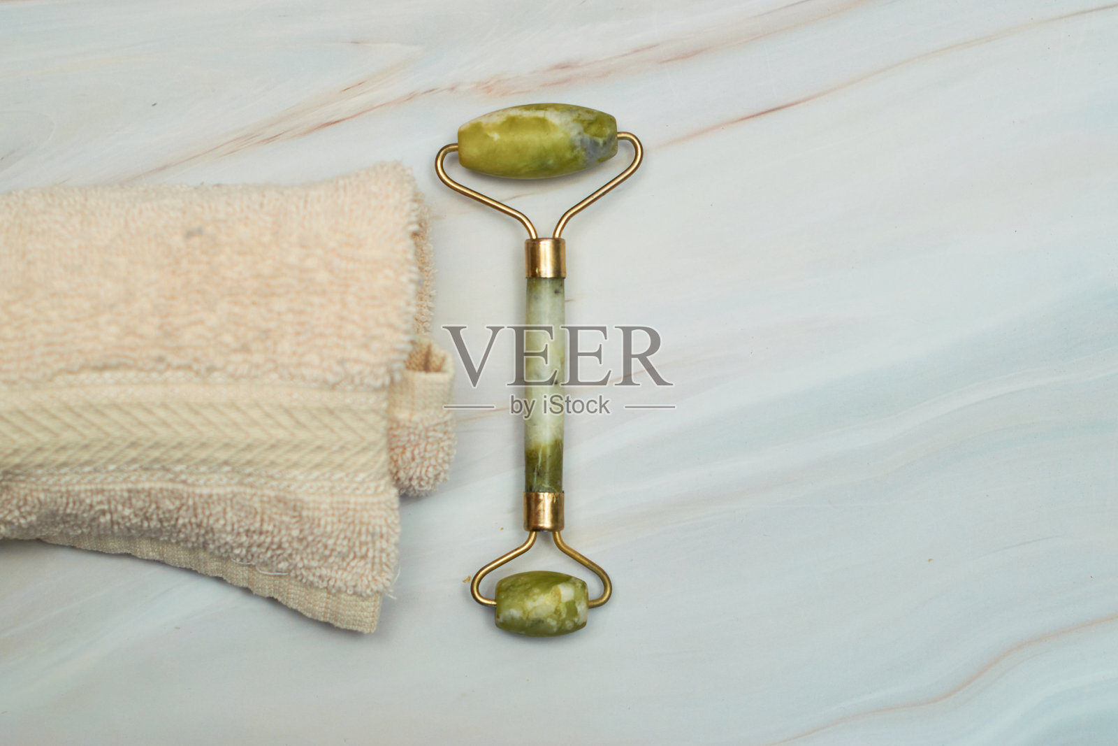 以大理石为背景，用碧玉滚轮和刮沙石按摩面部。照片摄影图片