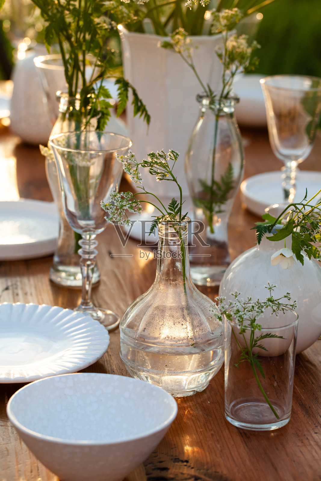 优雅的婚礼餐桌上装饰着白色的盘子，玻璃花瓶上插着鲜花。喜庆气氛，豪华派对。夕阳西下，明媚的夏夜。近距离、细节照片摄影图片