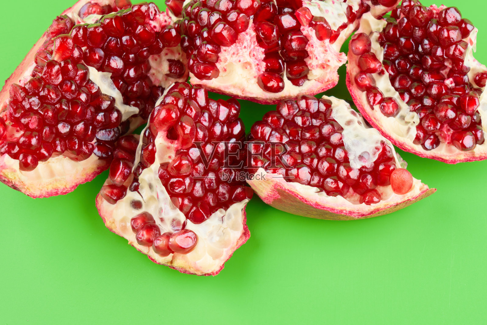 红色成熟的新鲜多汁的石榴切片孤立在绿色的背景上照片摄影图片