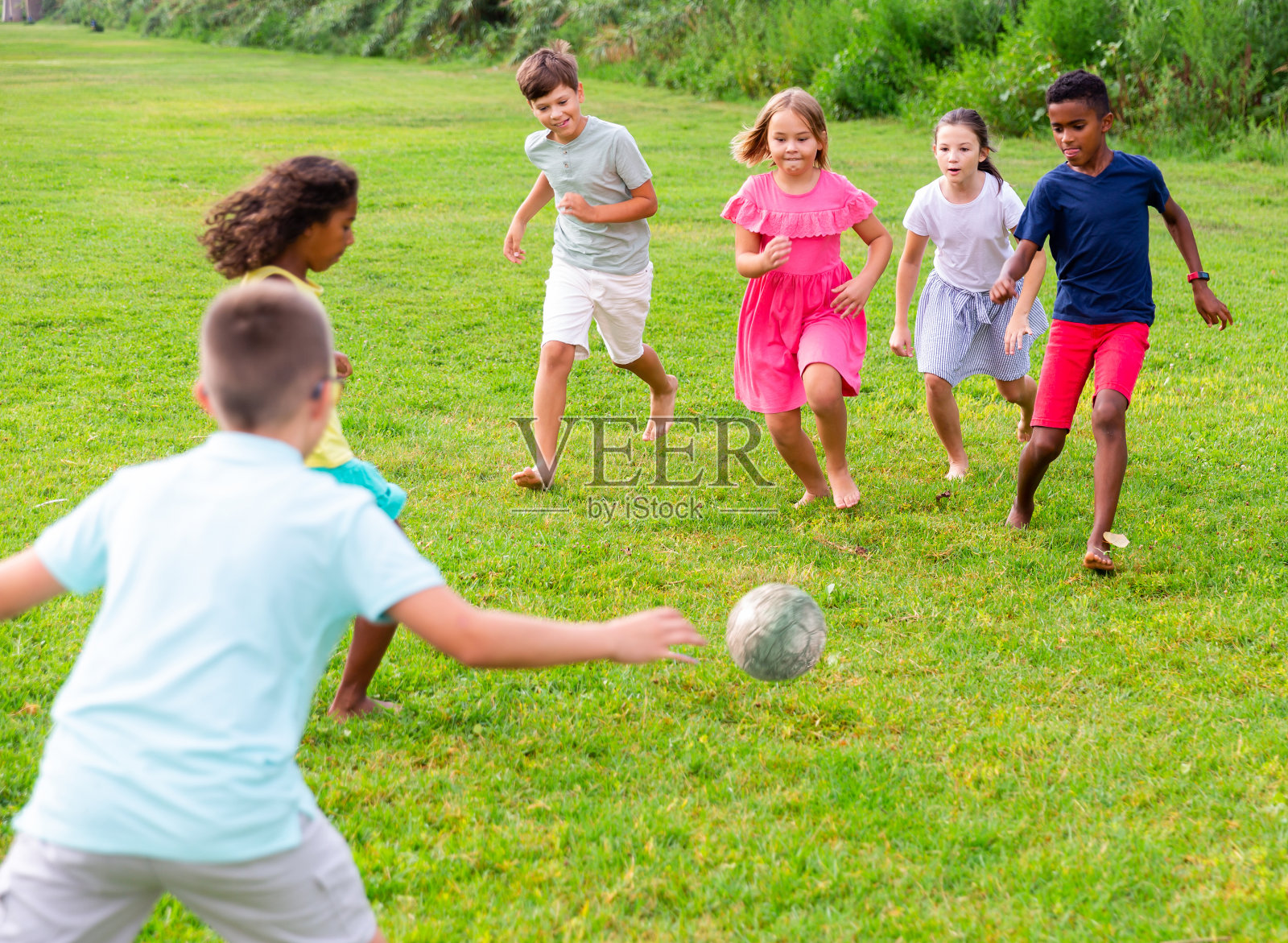 快乐的十几岁的女孩和男孩在绿色的草坪上踢足球照片摄影图片