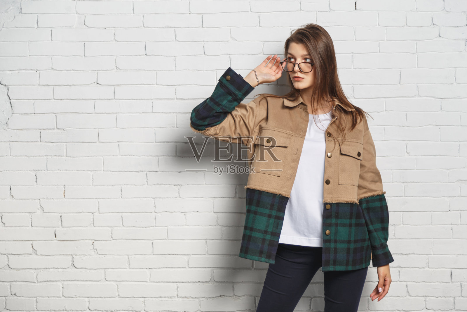 戴着眼镜的年轻时髦女人在白色砖墙上。画像与copyspace照片摄影图片