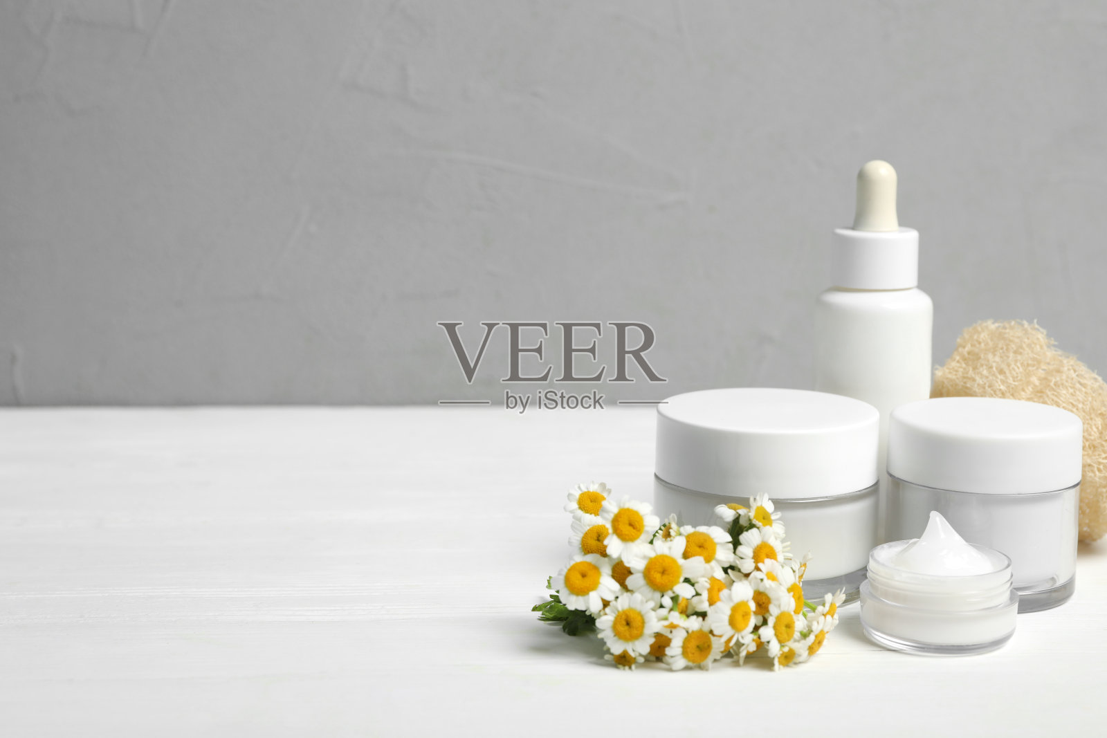 套装化妆品，洋甘菊和丝瓜在白色的桌子上对灰色的背景。空间的文本照片摄影图片