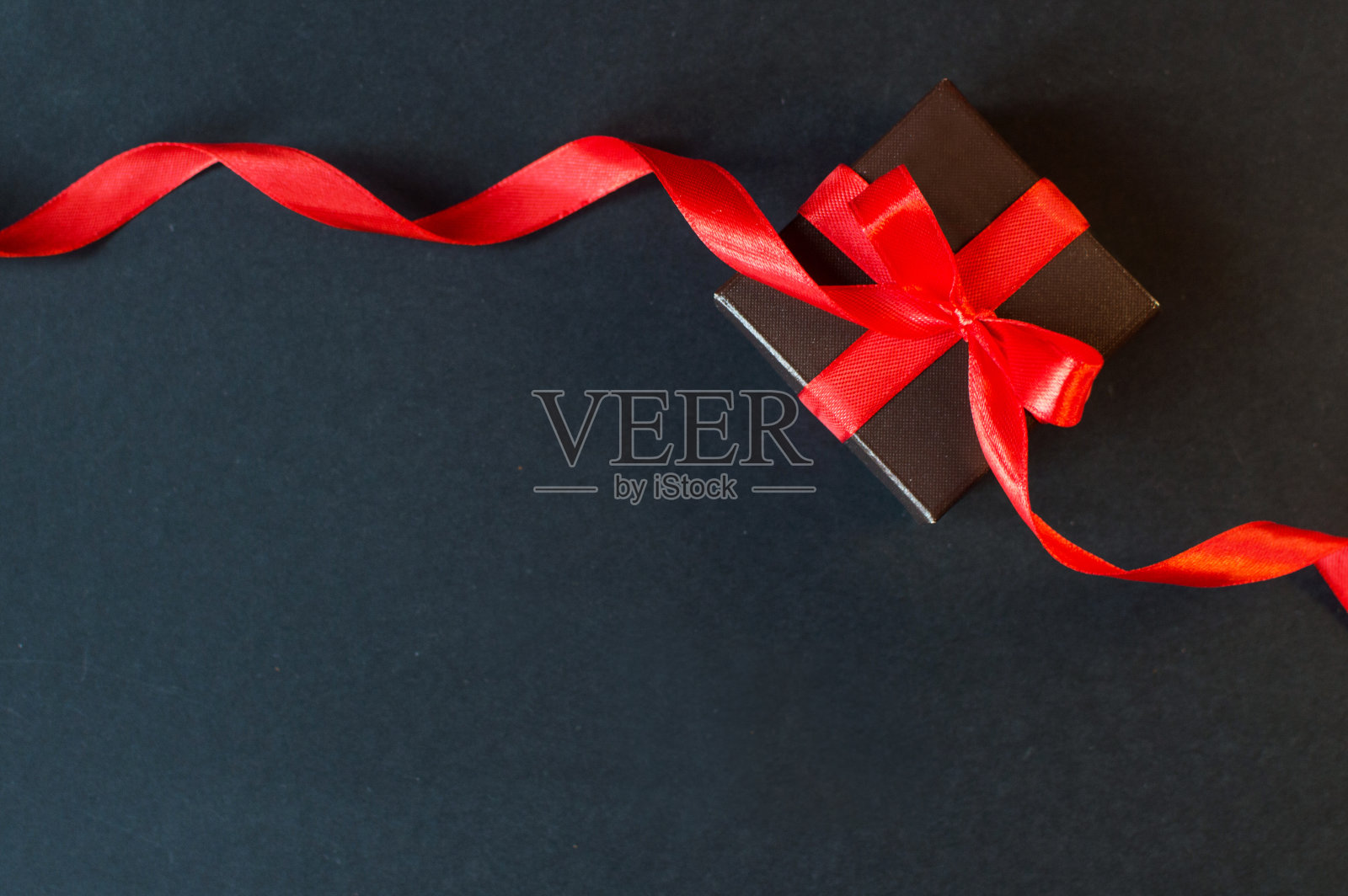 黑色星期五-黑色的礼品盒与一个红色蝴蝶结在黑暗的背景。照片摄影图片