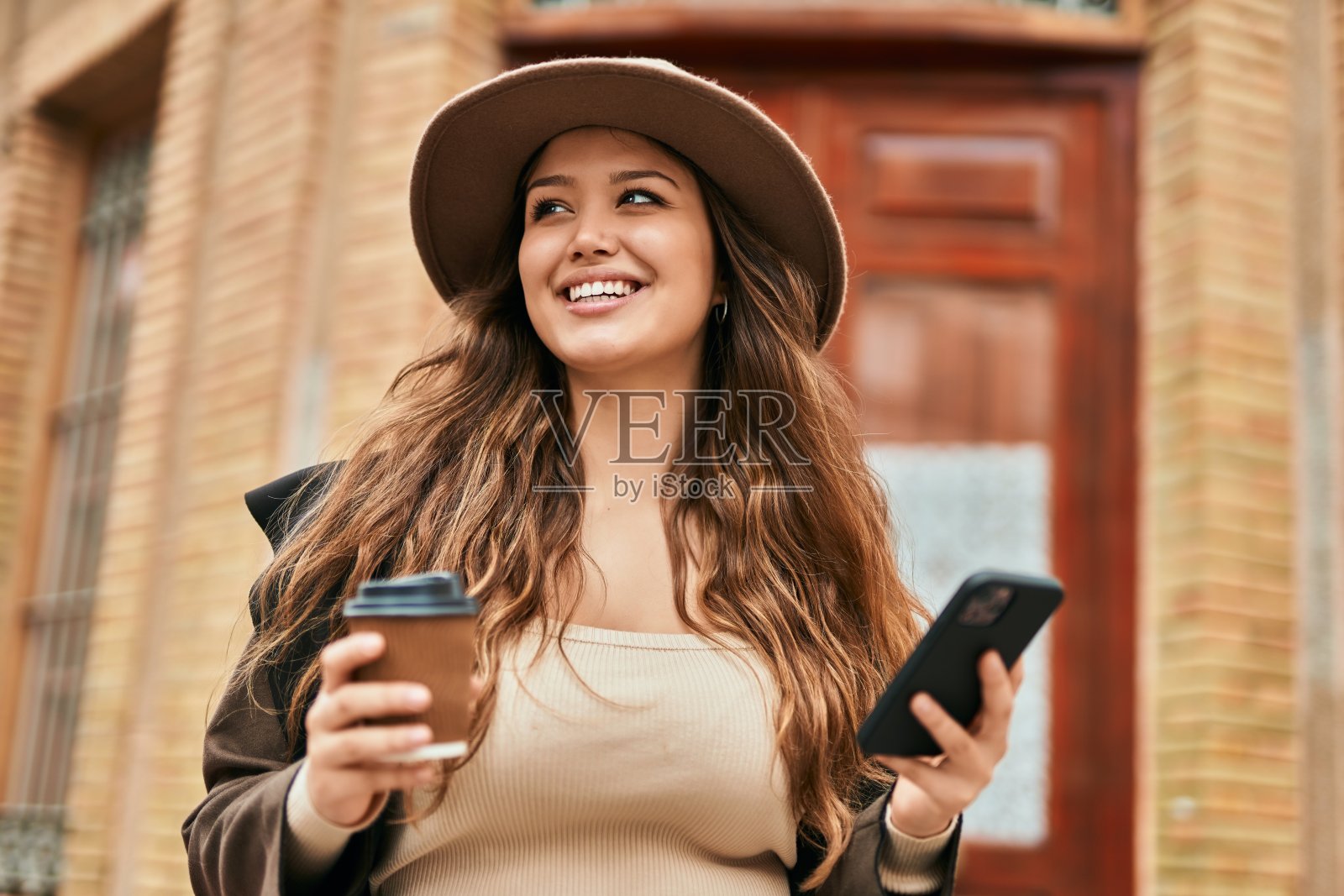 年轻的西班牙裔女游客在城市里用智能手机喝咖啡。照片摄影图片