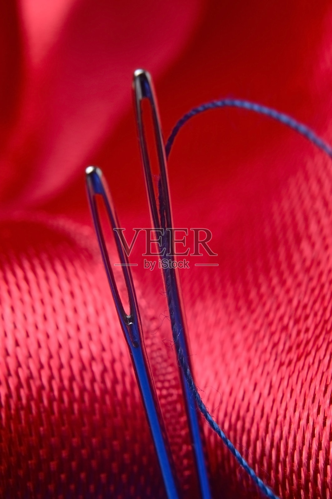 两根绣着蓝色线的缝衣针，背景是红色的织物。特写镜头。照片摄影图片