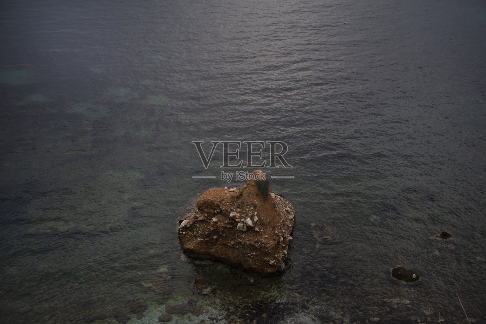 海边有一块巨大的石头，海里有波浪。阳光反射在海面上照片摄影图片