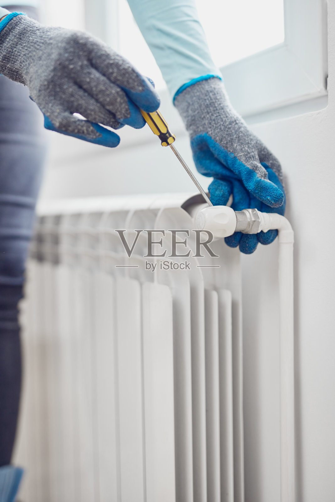戴着手套的杂工在家里修理和排出中央供暖燃气散热器系统的空气。照片摄影图片