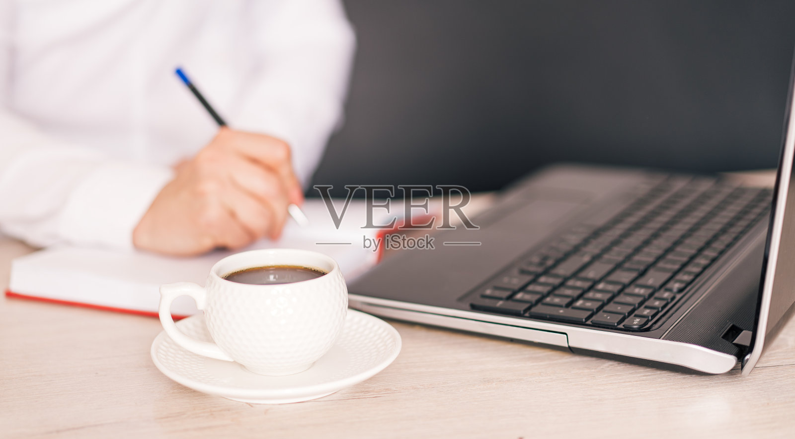 女人在笔记本电脑和一杯咖啡前用笔在笔记本上写字照片摄影图片
