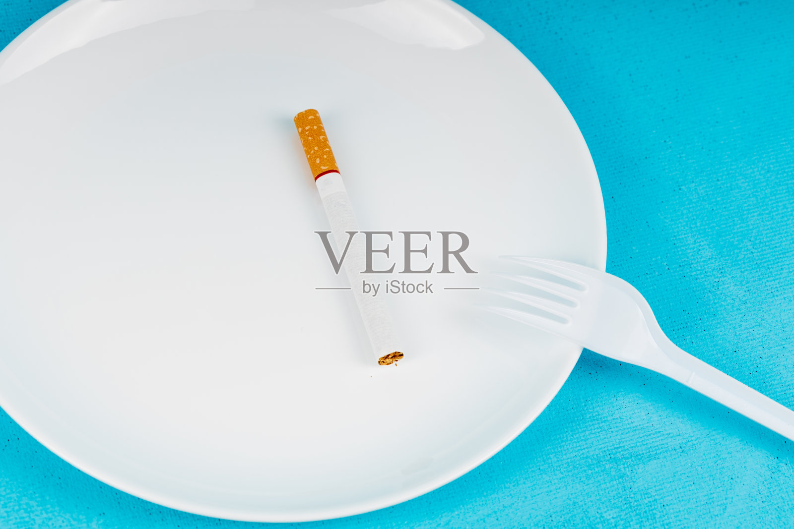 叉子和香烟代替了盘子上的食物，背景是蓝色的。用香烟代替吃的概念照片摄影图片