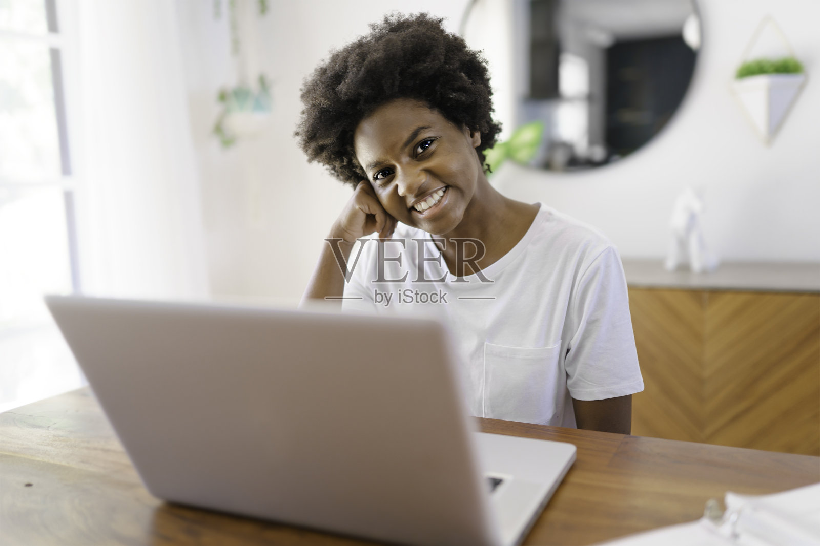 微笑的年轻非洲女企业家坐在家里的厨房桌子上，用笔记本电脑在线工作照片摄影图片