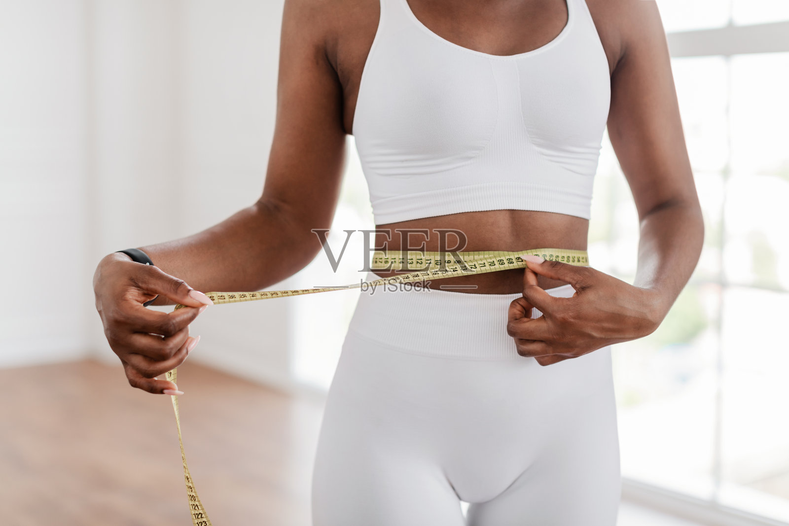 黑人妇女用胶带量腰。节食减肥的概念照片摄影图片