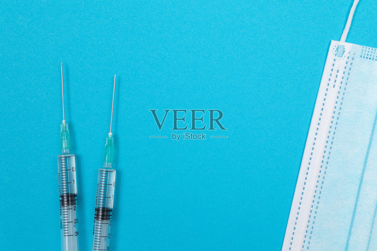 带医用口罩的注射器放在蓝色桌子上-平放照片摄影图片