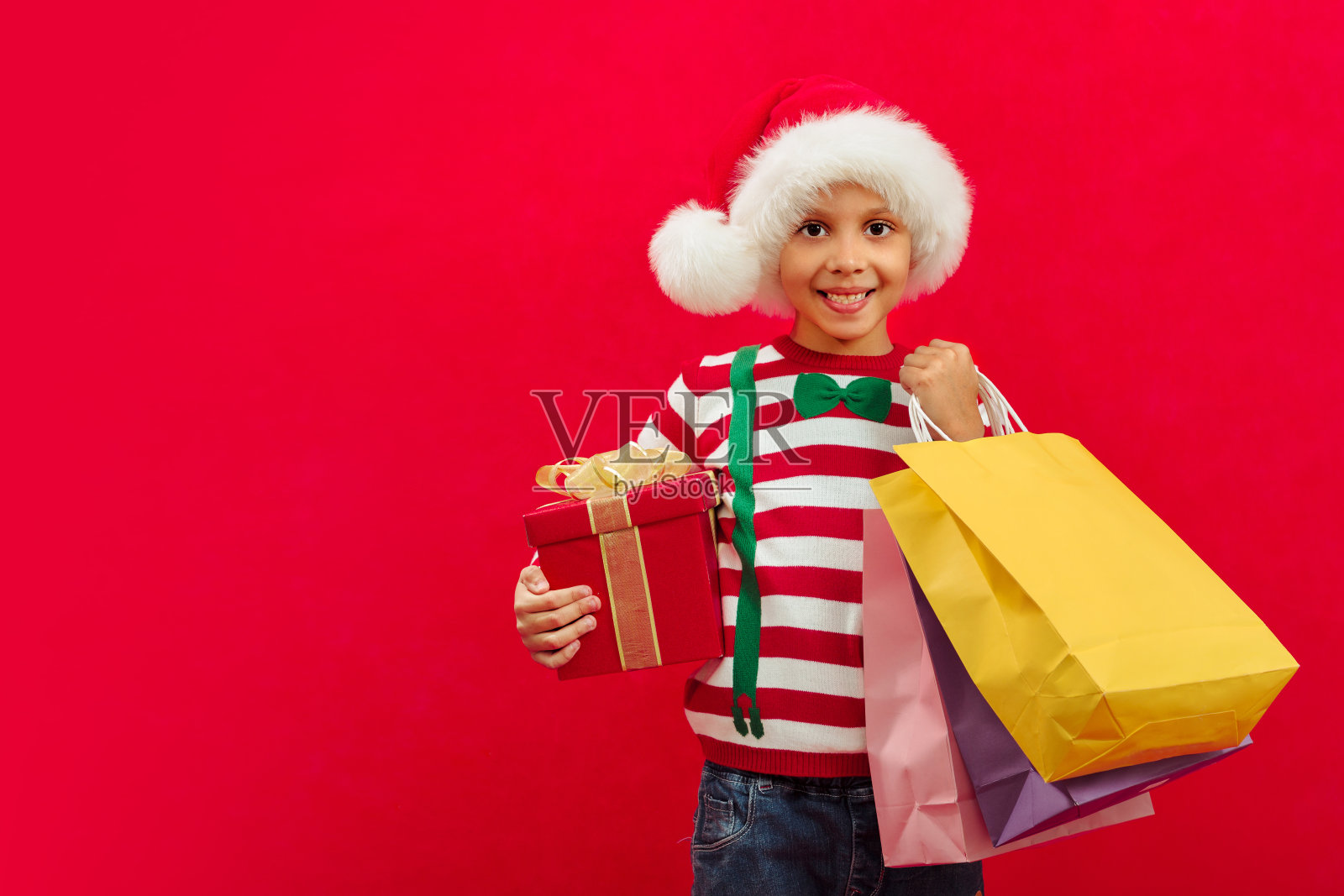 一个非裔美国男孩戴着圣诞老人的帽子，手里拿着礼盒和纸袋送给朋友照片摄影图片