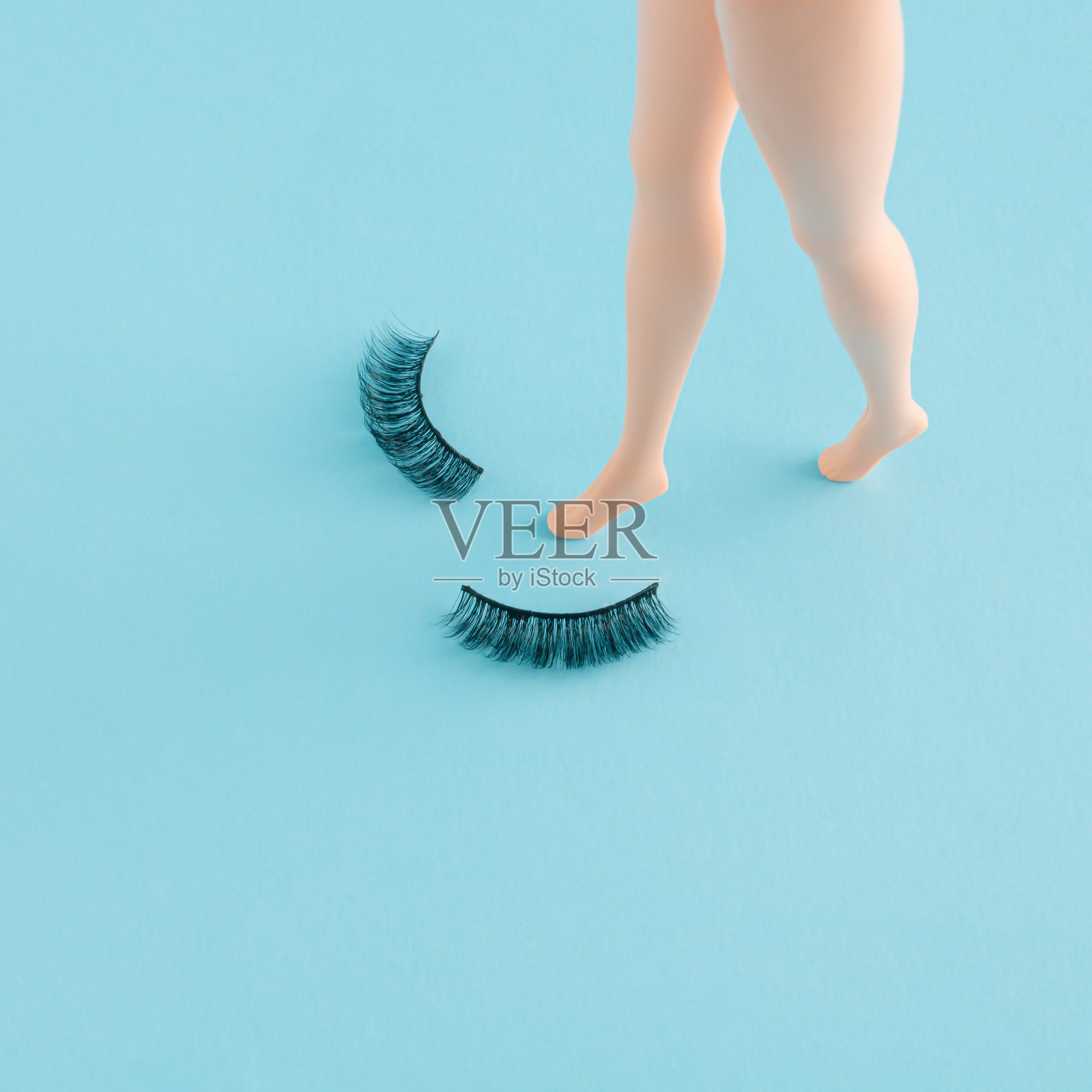 有创意的最小组成与娃娃腿和蓝色背景上的睫毛。照片摄影图片