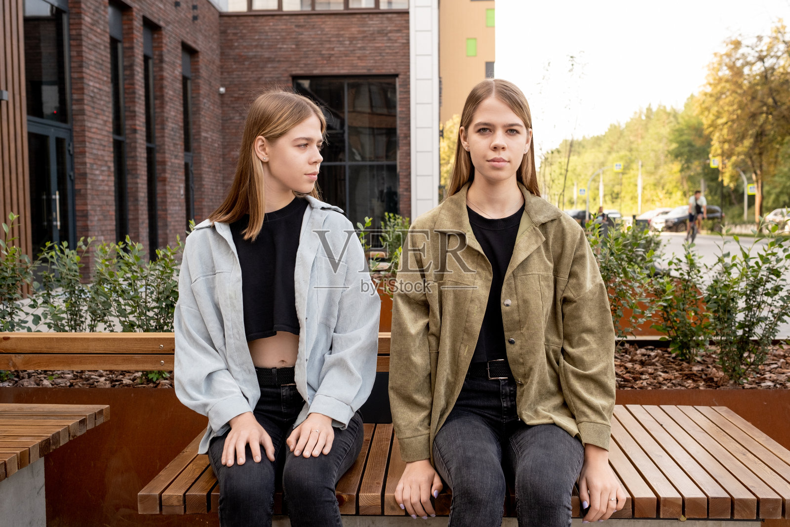 其中一对双胞胎坐在她妹妹旁边的长凳上看着你照片摄影图片