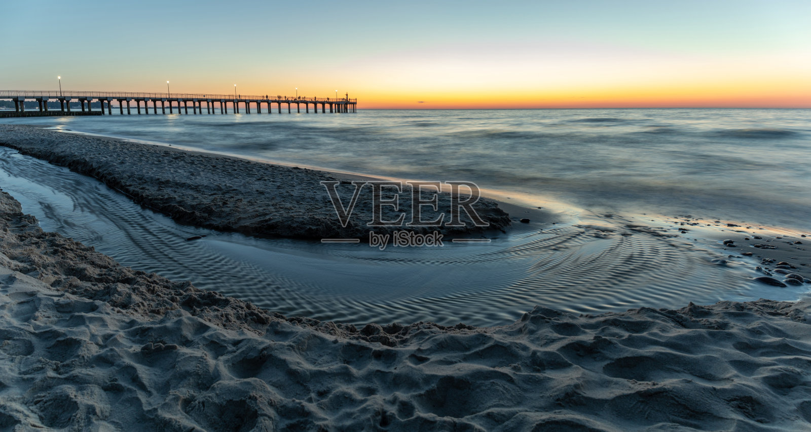 海滩上一条小河风景如画，人们在码头上散步，海边日落，全景照片摄影图片