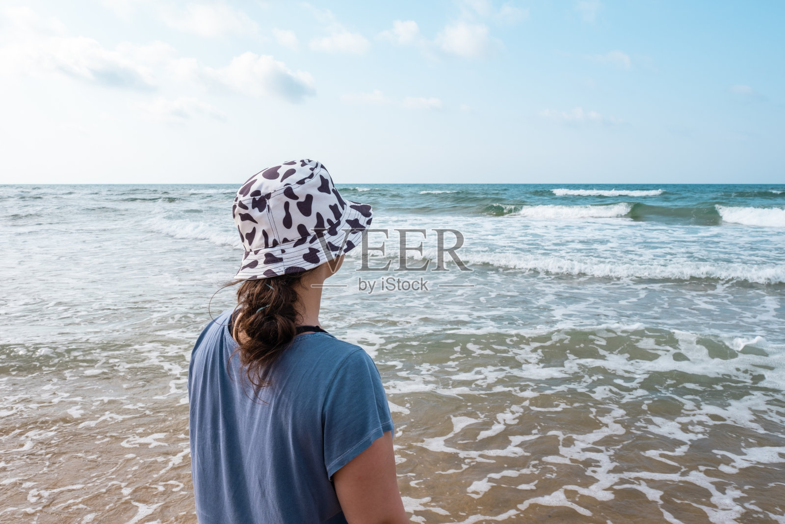 一位戴着水桶太阳帽的年轻女士站在海边照片摄影图片