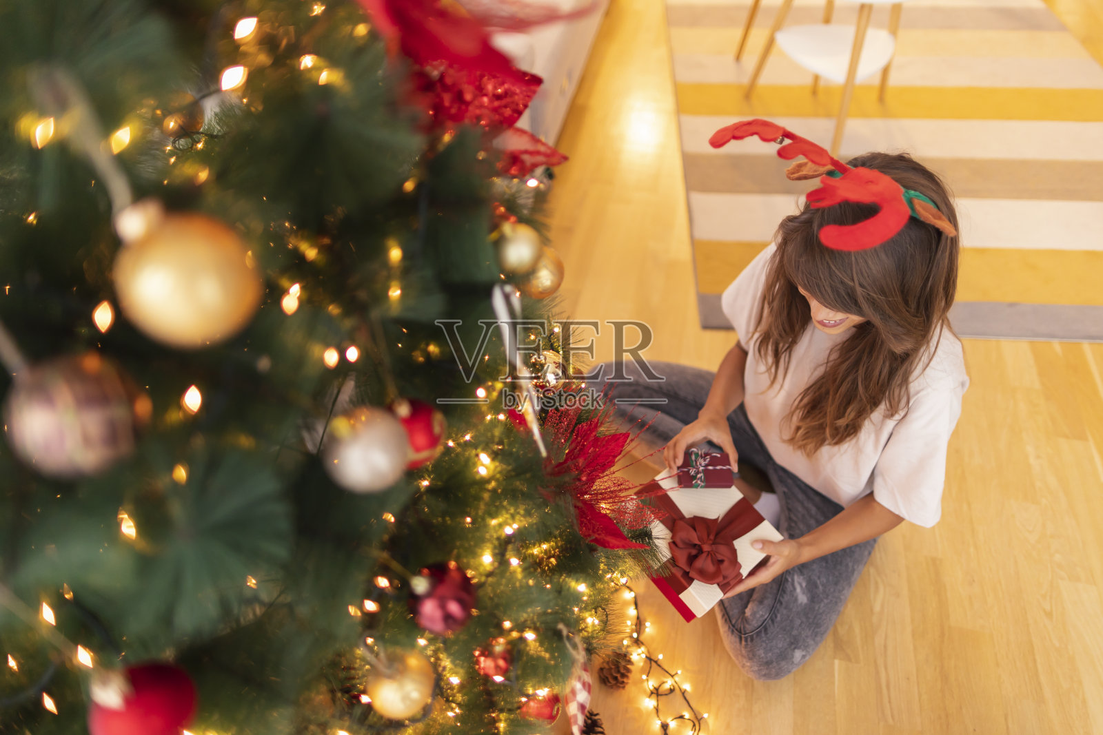女人坐在圣诞树旁，手里拿着圣诞礼物照片摄影图片