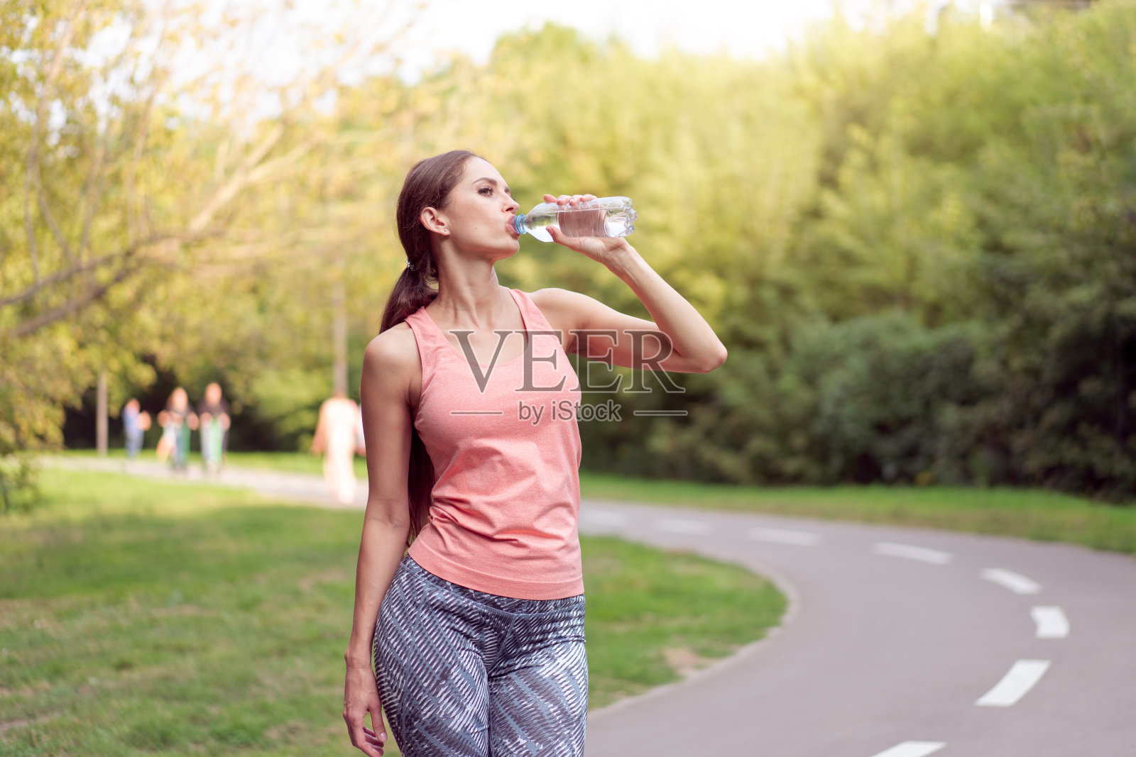 女运动员站在夏季公园的跑道上，跑步锻炼后喝水照片摄影图片