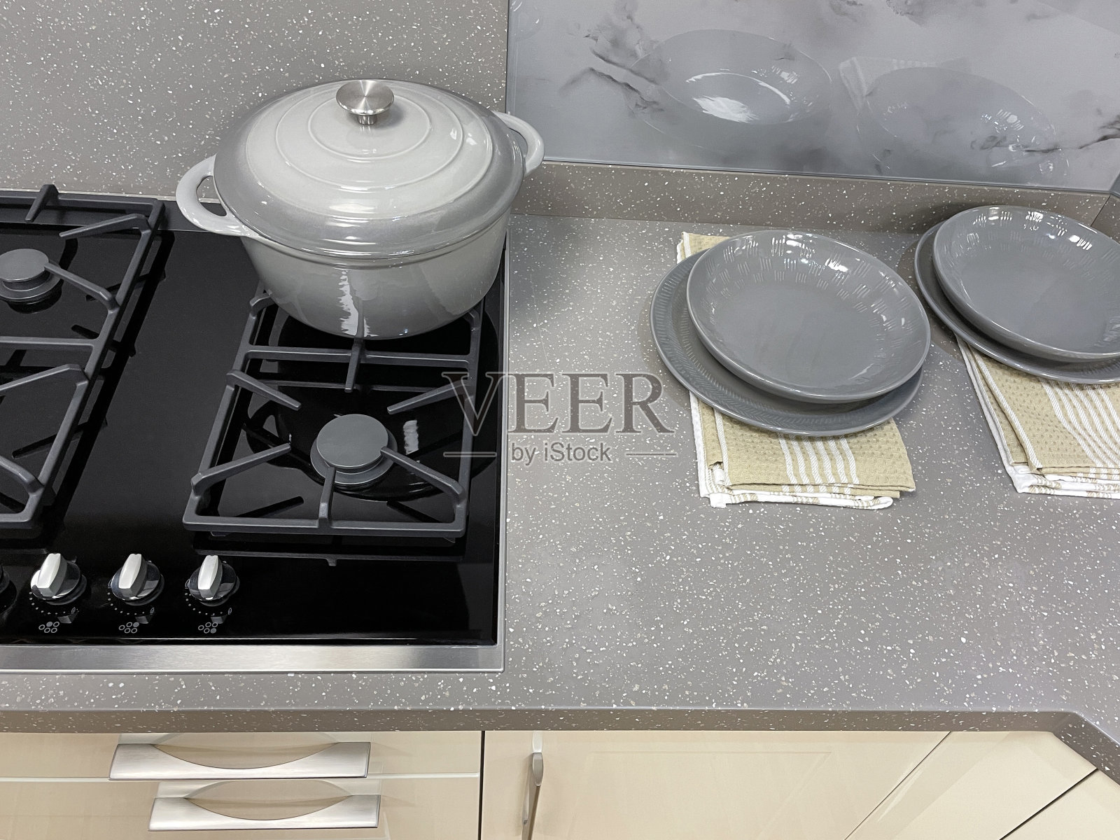 近景现代厨房与光滑，奶油抽屉，墙壁和地板橱柜，灰色可丽耐厨房柜台镶嵌玻璃陶瓷燃气灶台，空灰色盘子，碗和砂锅菜，高架视图照片摄影图片