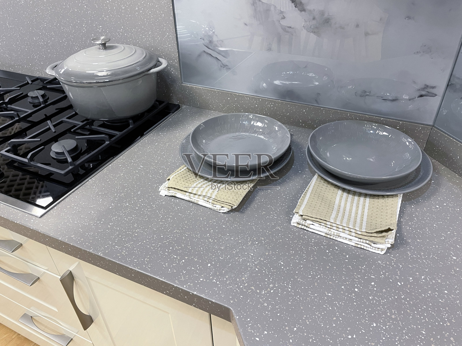 近景现代厨房与光泽，奶油抽屉，墙壁和地板橱柜，灰色可丽耐厨房柜台镶嵌玻璃陶瓷燃气灶台，空灰色盘子，碗和砂锅菜照片摄影图片