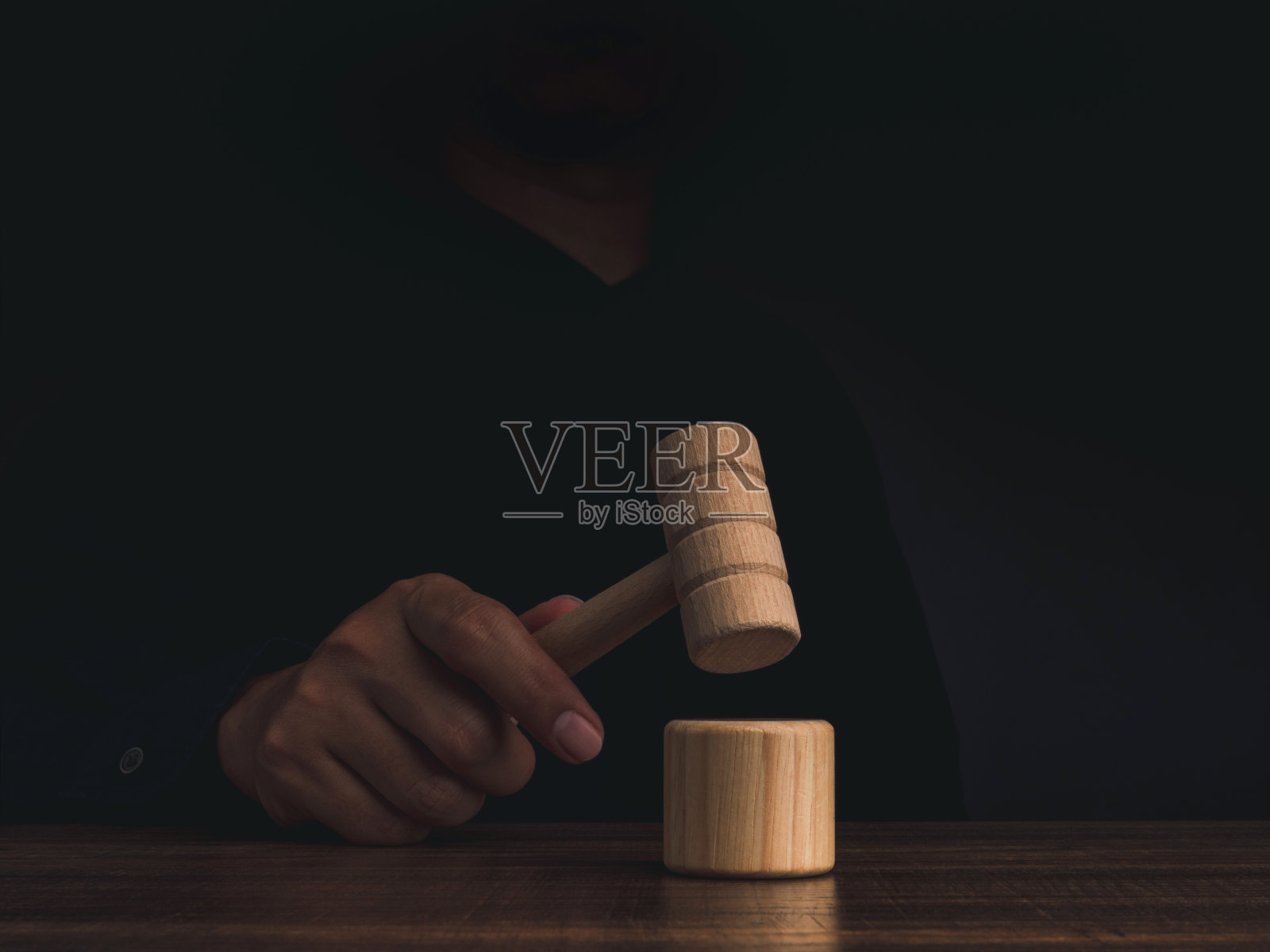 手中握着木制法官槌，在深色背景的木桌上敲击，象征公正、法律和反腐败照片摄影图片