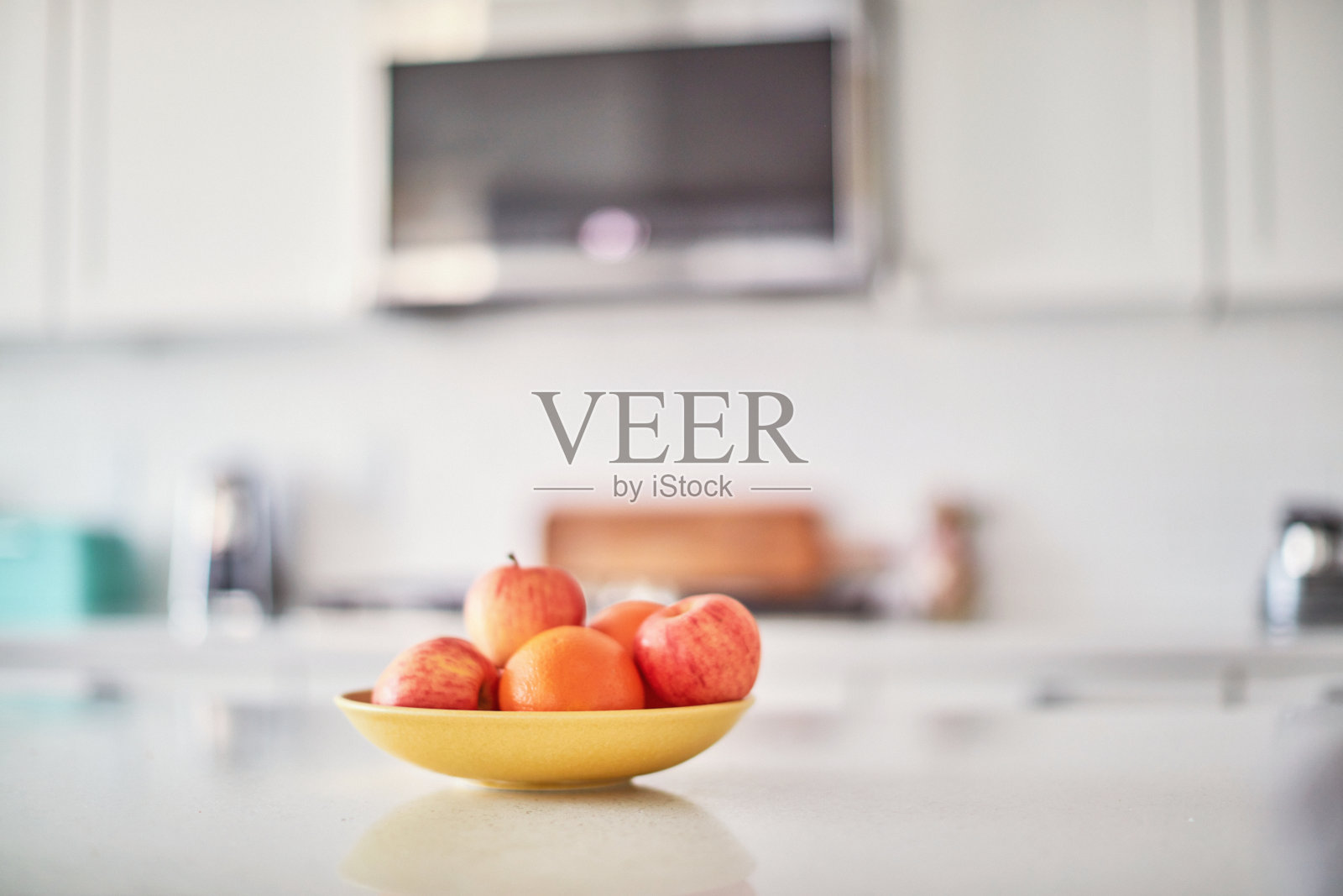 在明亮的白色现代厨房里，一个小岛上，一个黄色的碗里盛着各式各样的水果照片摄影图片