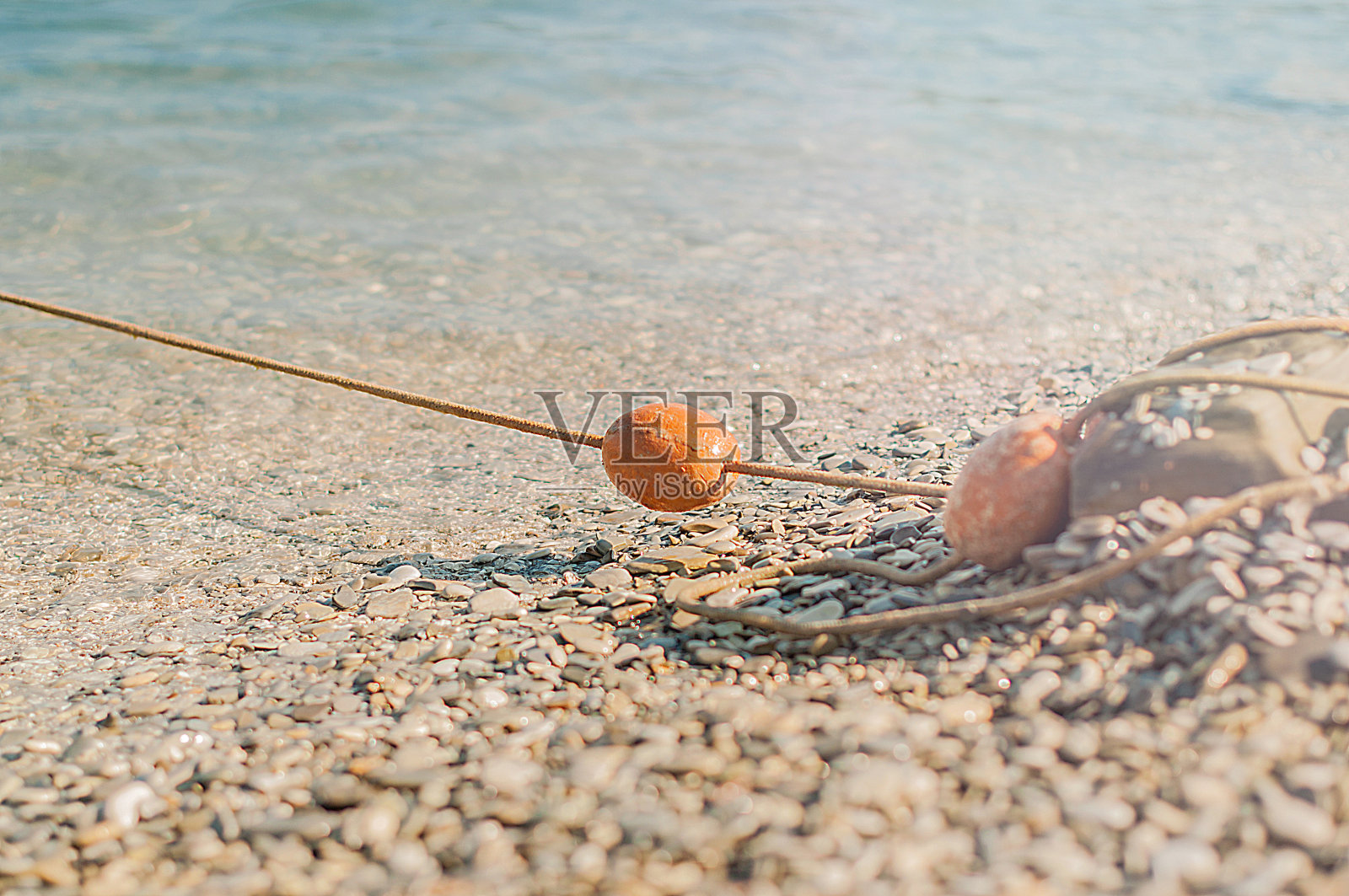旧的红色泡沫聚苯乙烯浮标在绳子上躺在海滩上。照片摄影图片