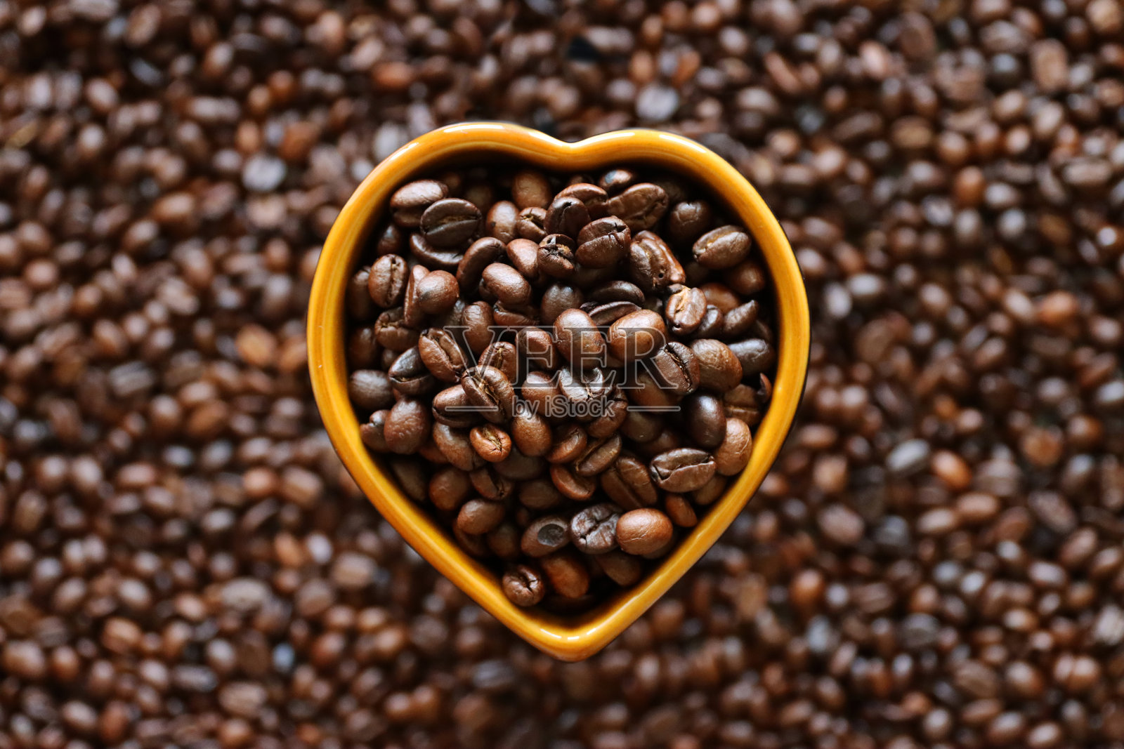 瓷器的特写图像，心形的杯子装满了黑咖啡豆坐在一堆烤咖啡豆的背景上，升高的视野照片摄影图片