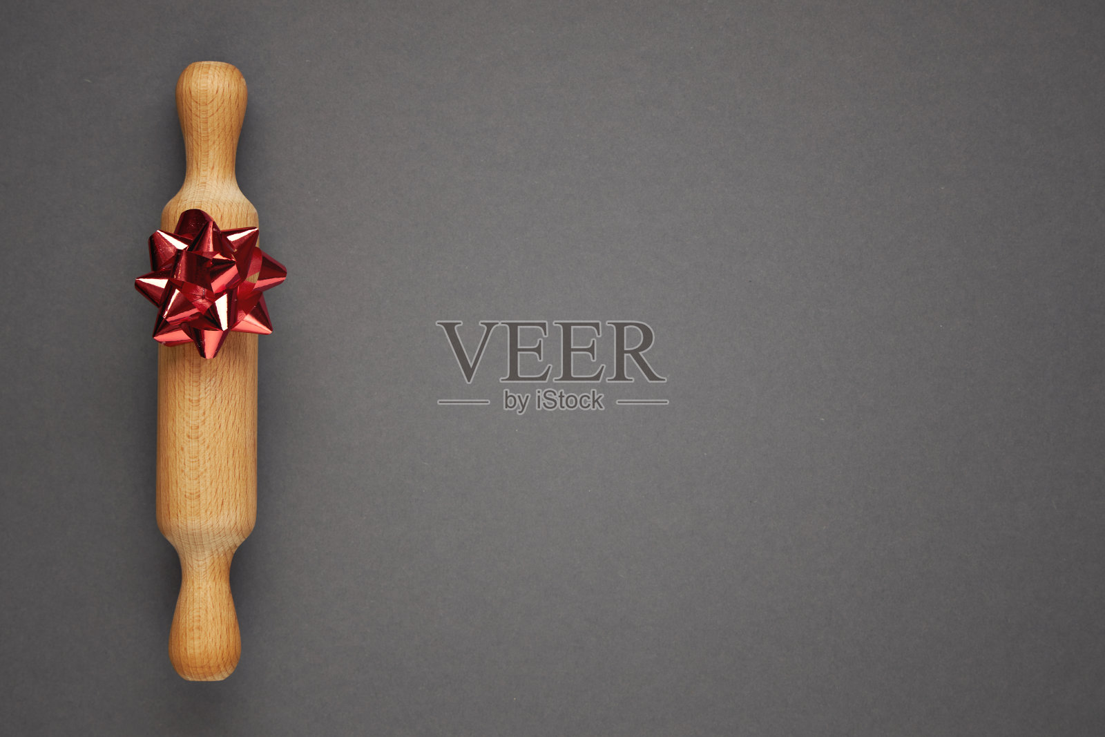 灰色背景上有一个红色蝴蝶结的木制擀面杖。节日烘焙的概念。照片摄影图片