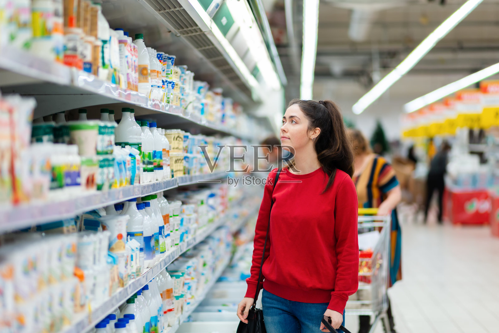 一个年轻漂亮的女人正在超市冰箱里的乳制品陈列柜里看。购物和消费主义的概念照片摄影图片