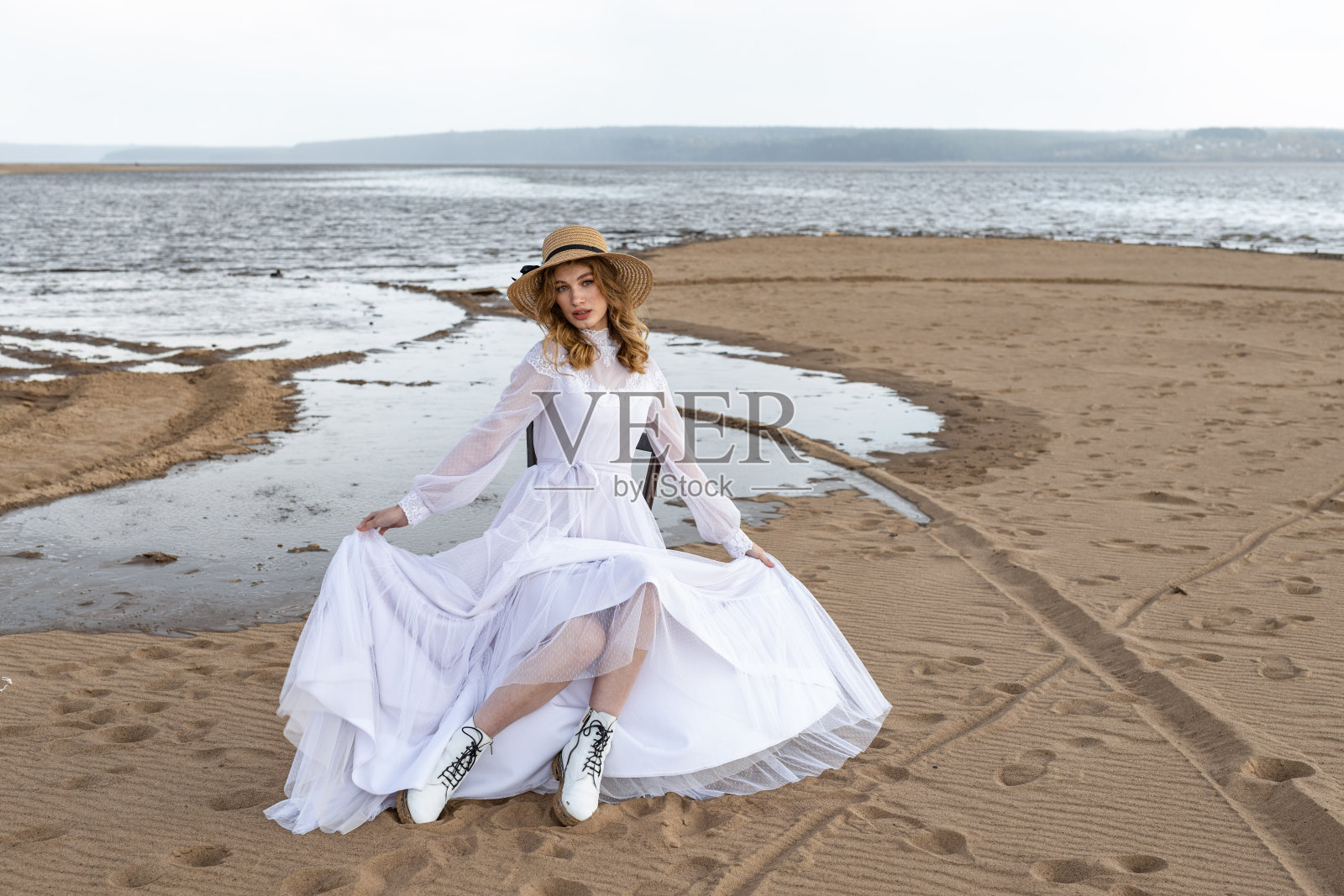 快乐的年轻女孩穿着白色的裙子站在河岸上。乌云中暴风雨的天空照片摄影图片