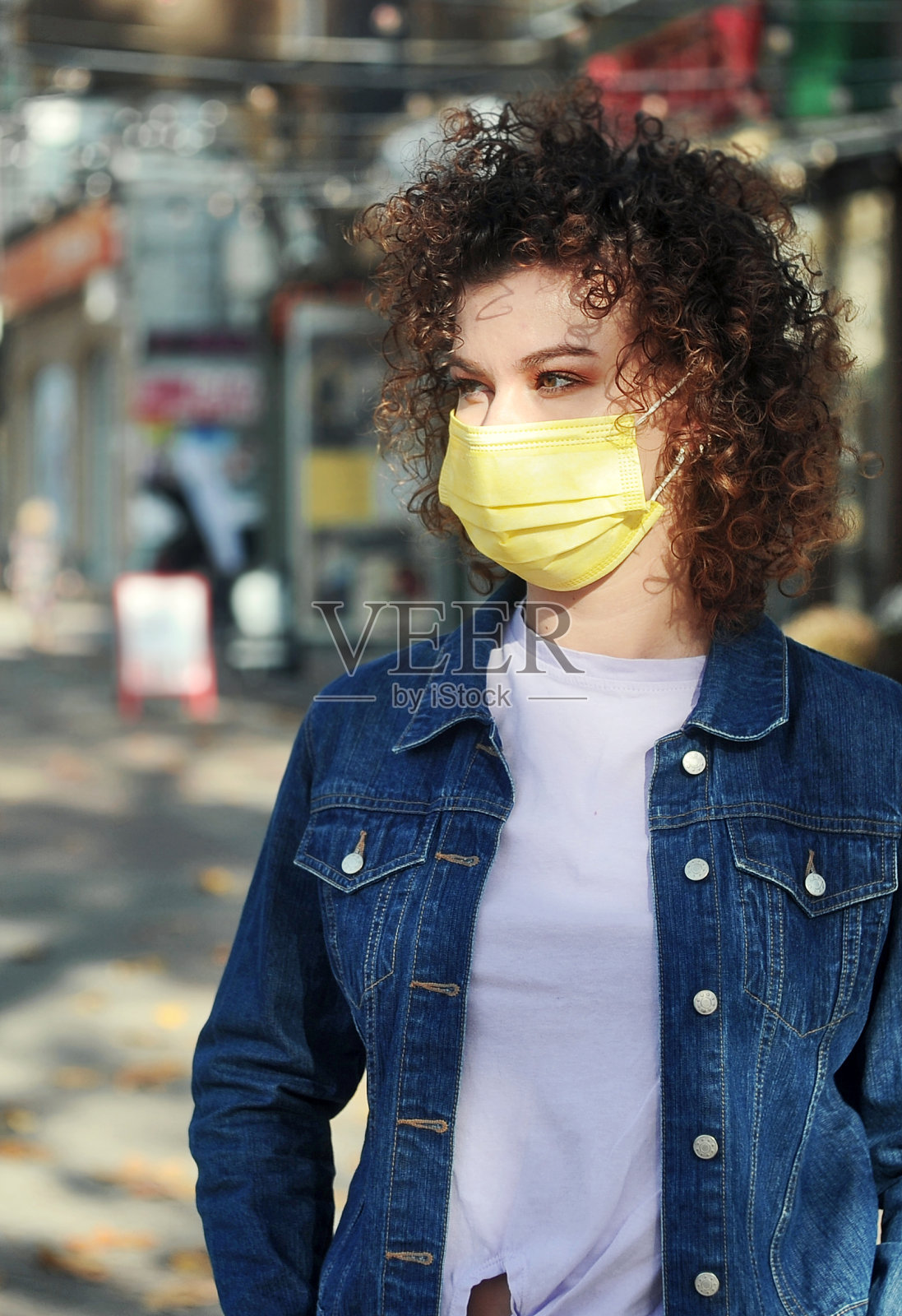 年轻美丽的卷发女人在保护面具喝咖啡在户外咖啡馆。照片摄影图片