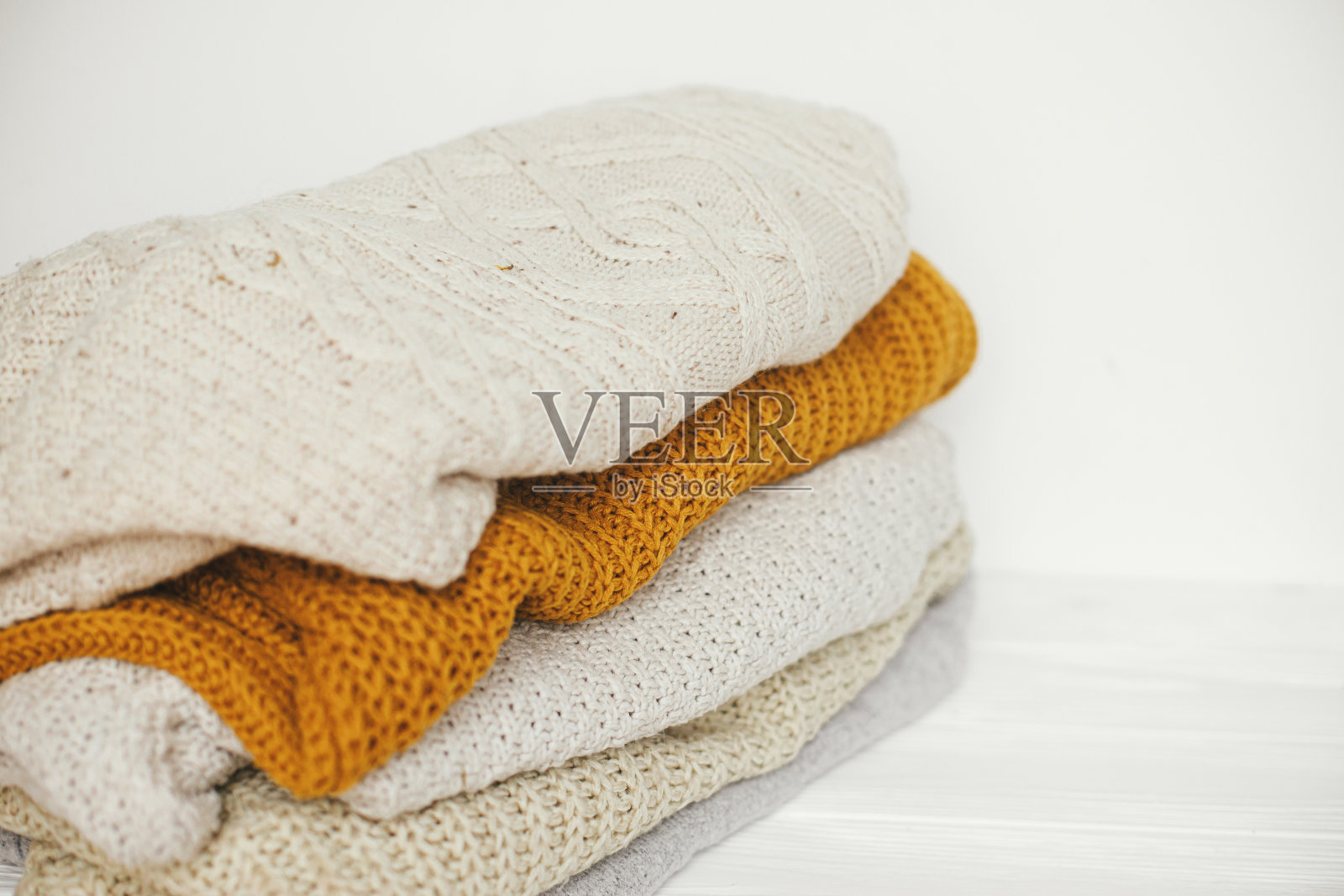 舒适的针织毛衣。白色、黄色和米色的针织毛衣堆在白色的斯堪的纳维亚房间里。你好,秋天。寒冷季节的时尚衣橱照片摄影图片