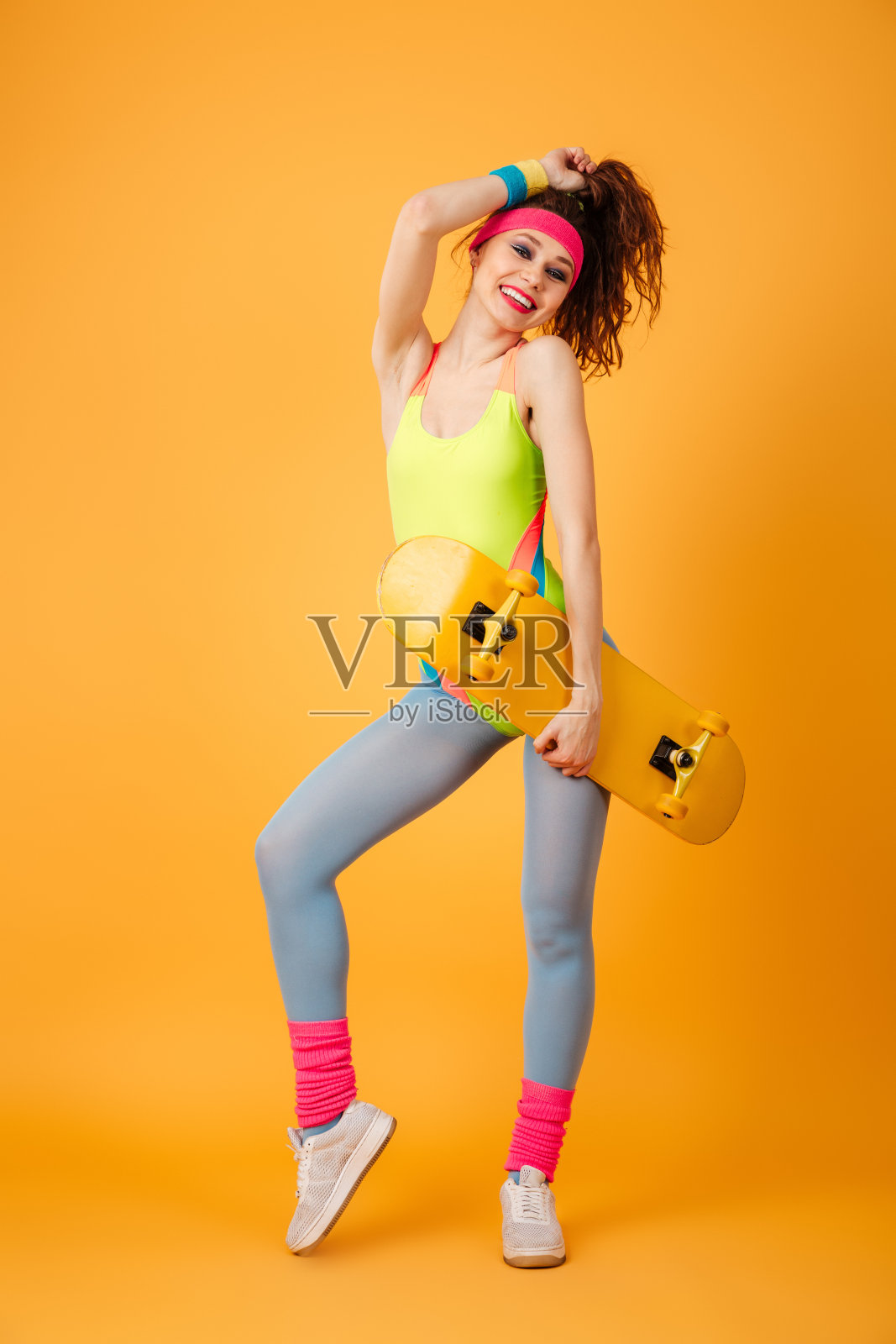 一个欢快的年轻女运动员站着，手里拿着滑板照片摄影图片