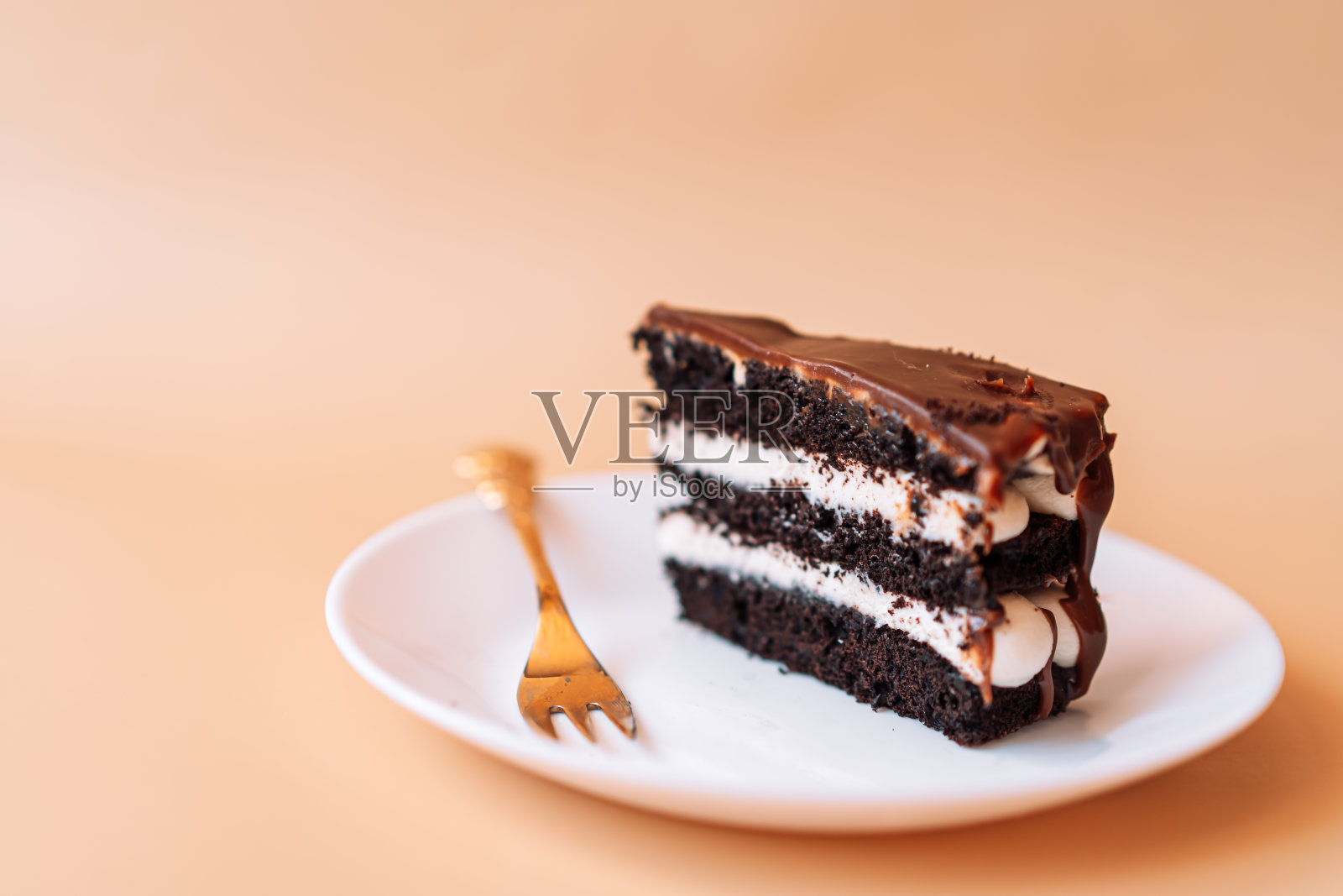 用金色的叉子把一块巧克力蛋糕放在盘子里照片摄影图片