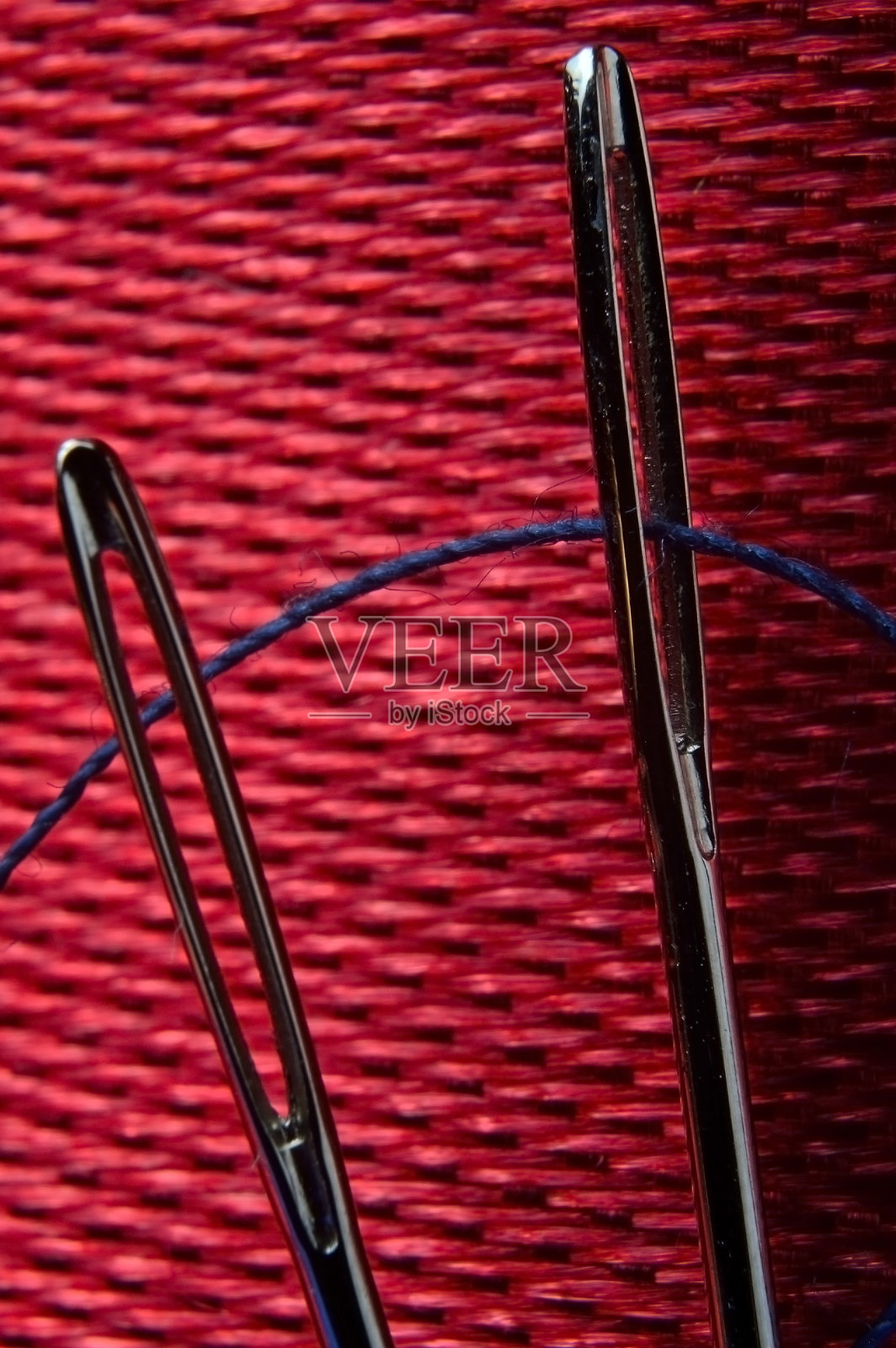 两根绣着蓝色线的缝衣针，背景是红色的织物。特写镜头。照片摄影图片