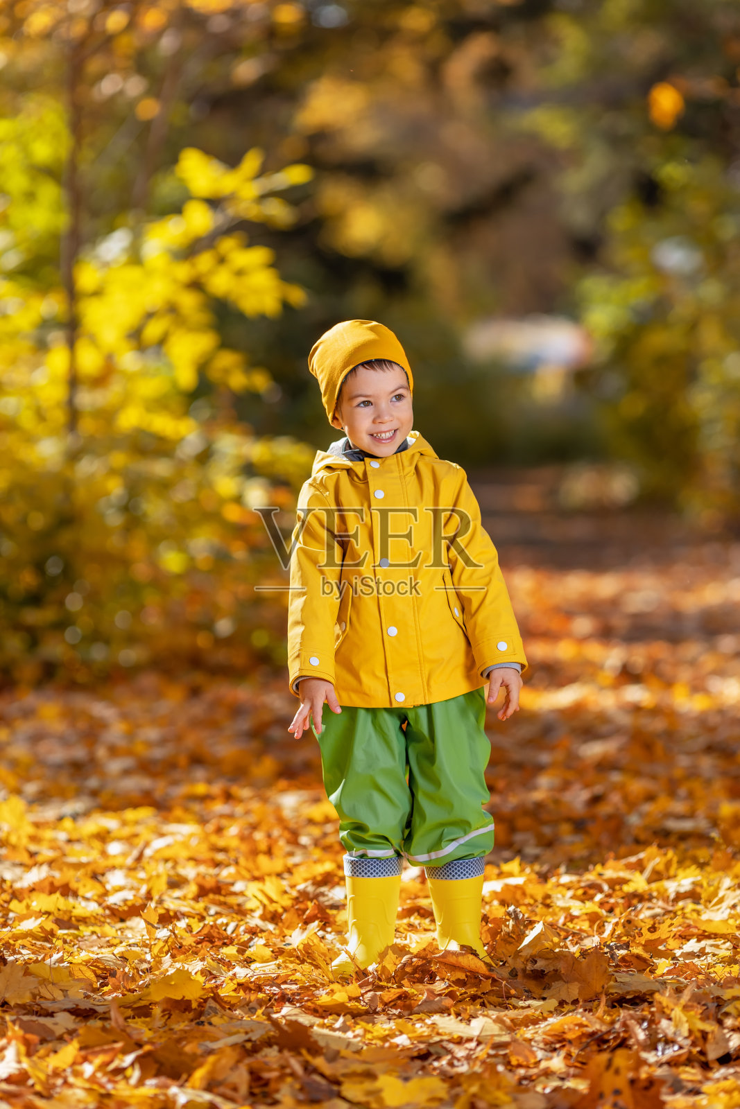 秋天公园里穿着黄色雨衣的微笑小男孩照片摄影图片